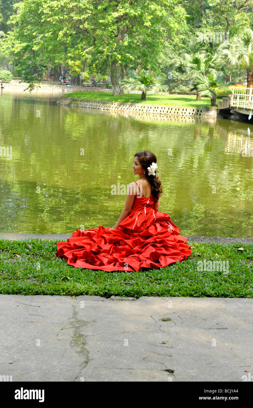 Braut in roten Brautkleid posieren für Outdoor-Fotografie am Bach Thao Park, Hanoi, Vietnam. Stockfoto