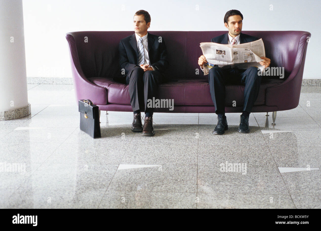 Zwei Geschäftsleute auf Sofa, einer Lesung Zeitung Stockfoto