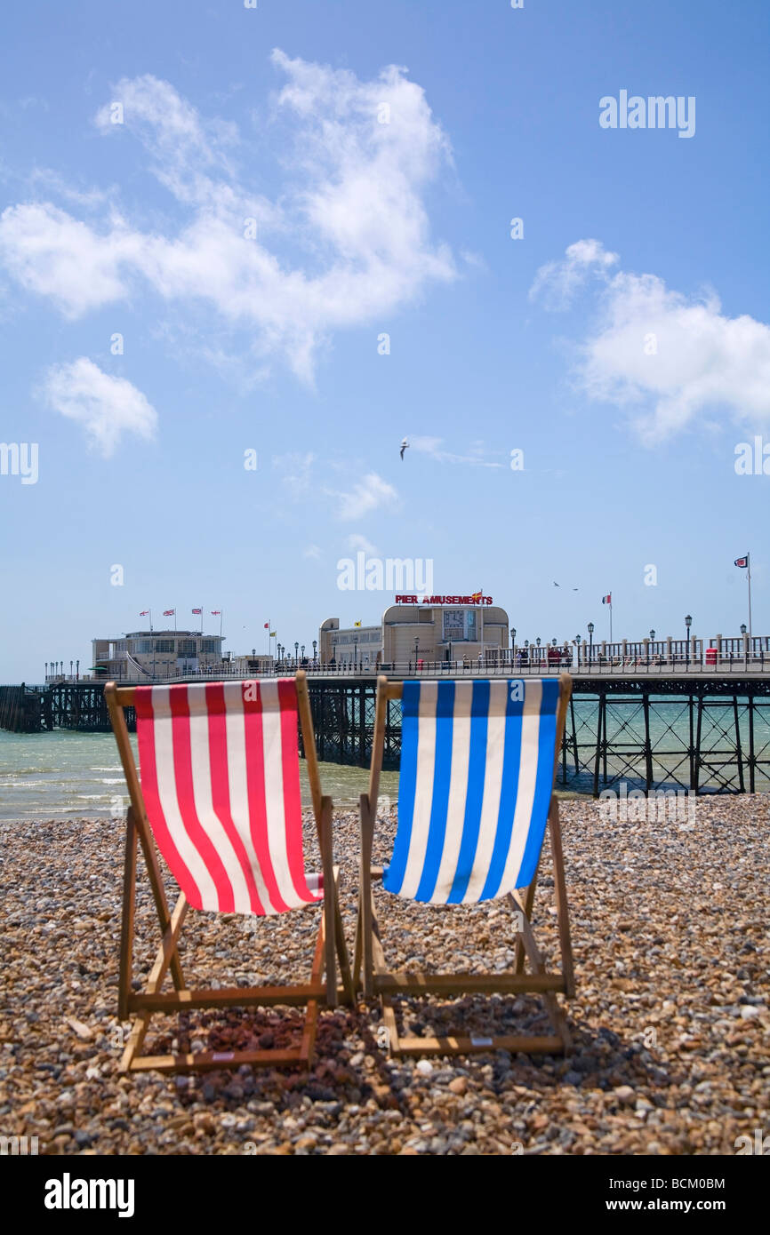 Rot-blau gestreifte Holzdeckstühle am Strand von Worthing mit Blick auf den Pier. West Sussex, Großbritannien Stockfoto