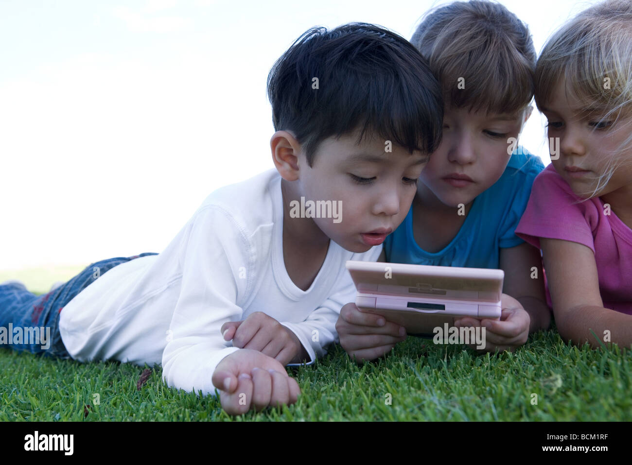 Drei Kinder auf dem Rasen liegen, spielen mit video Spiel, Nahaufnahme Stockfoto