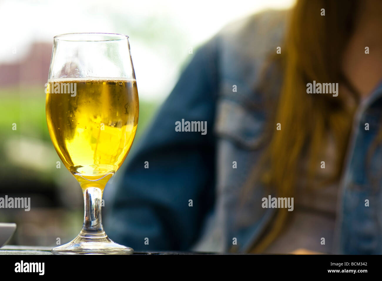 Glas Bier auf Tisch, junge Frau im Hintergrund Stockfoto
