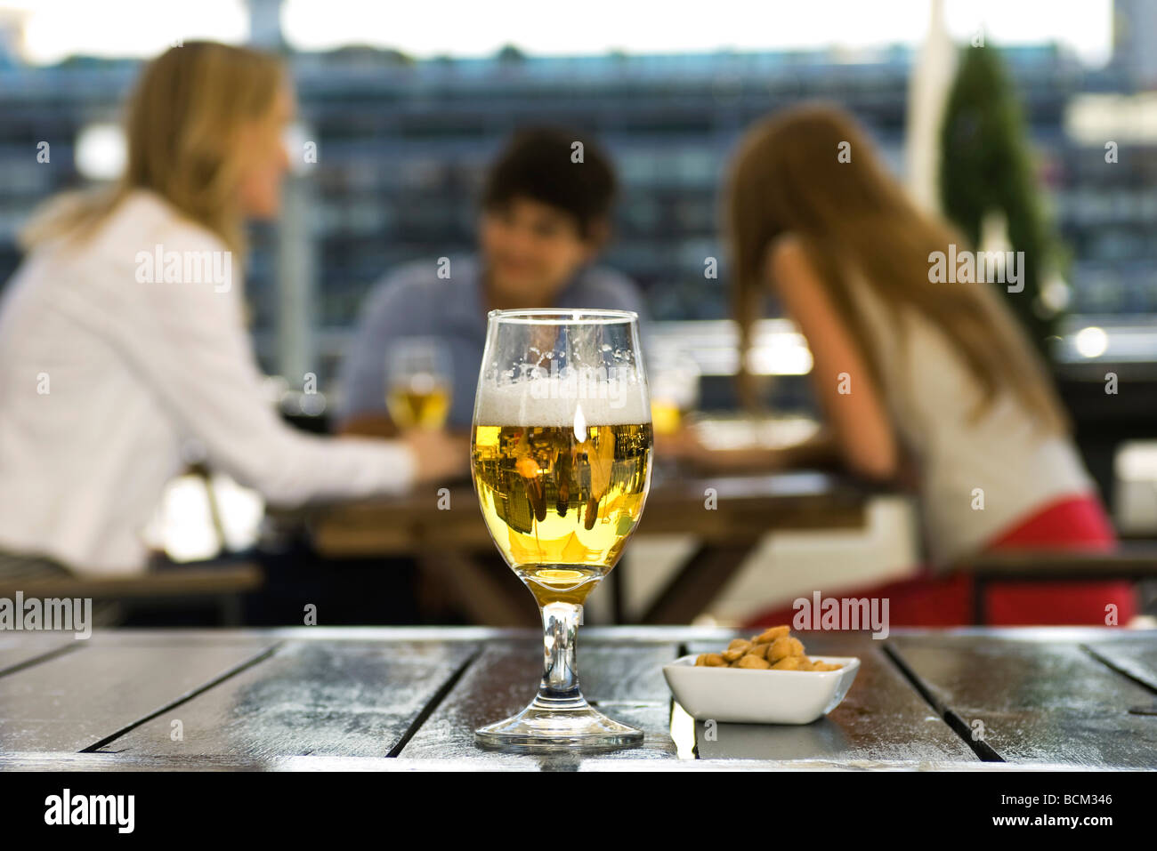 Glas Bier und Schale mit Erdnüssen auf Café-Tisch, Freunde im Chat im Hintergrund Stockfoto