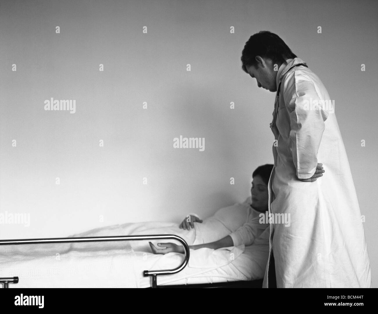 Frau liegend im Krankenbett, Arzt stehen an ihrer Seite Stockfoto