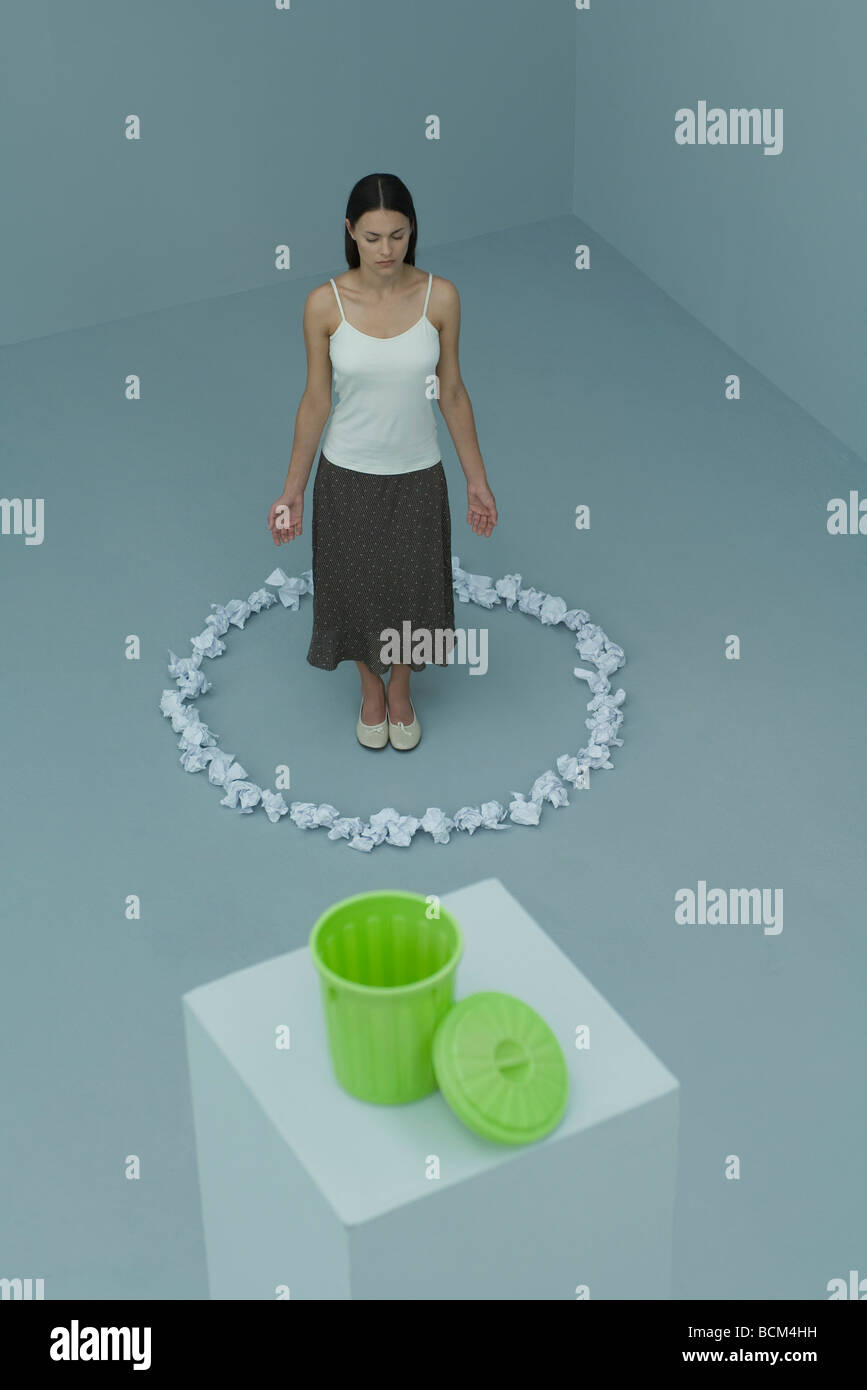 Frau im inneren Kreis von Papierkugeln, Augen geschlossen, Mülleimer im Vordergrund stehen Stockfoto
