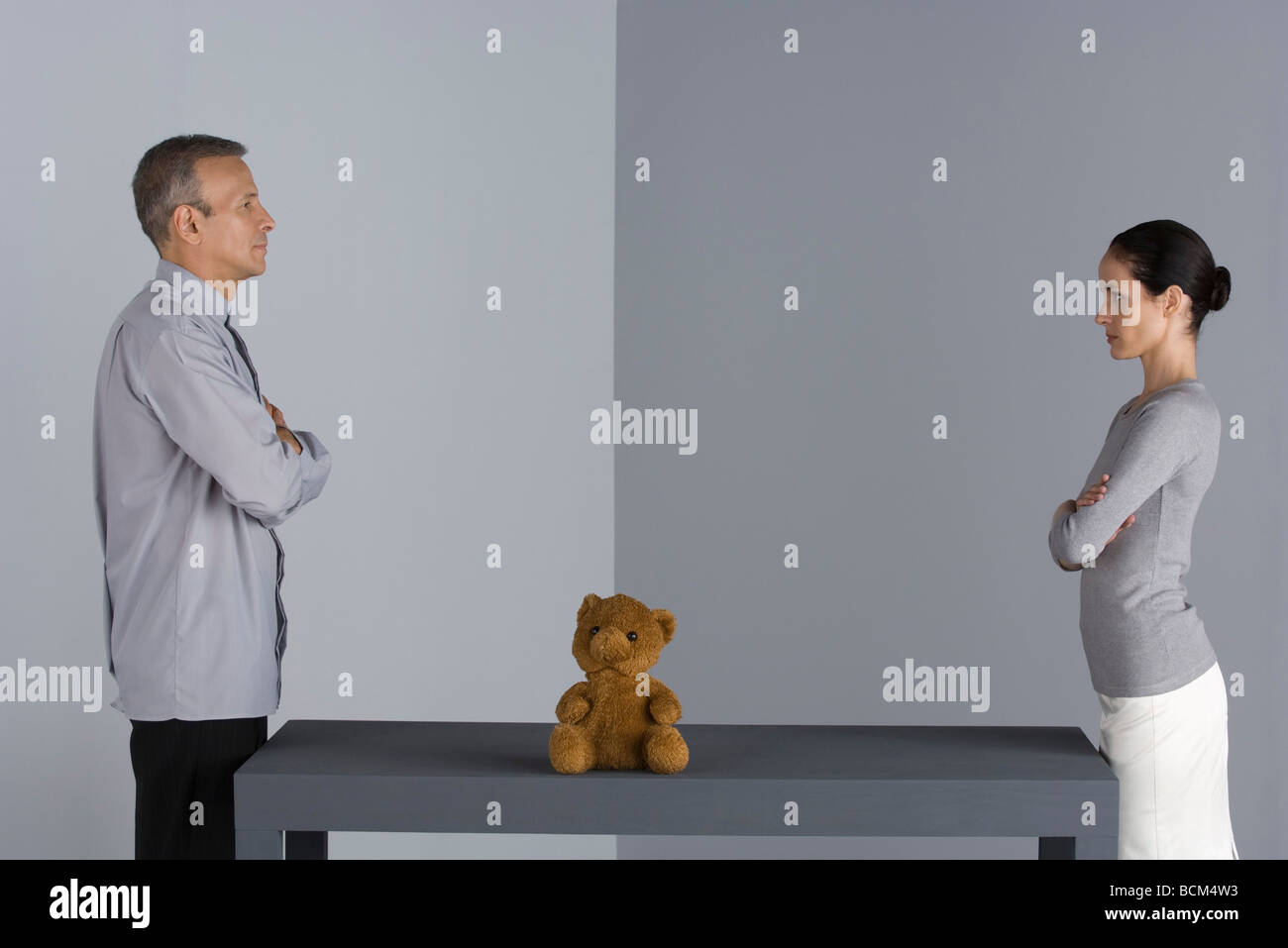 Paar von Angesicht zu Angesicht am Tisch stehen, verschränkt Arme, Teddybär zwischen Ihnen Stockfoto