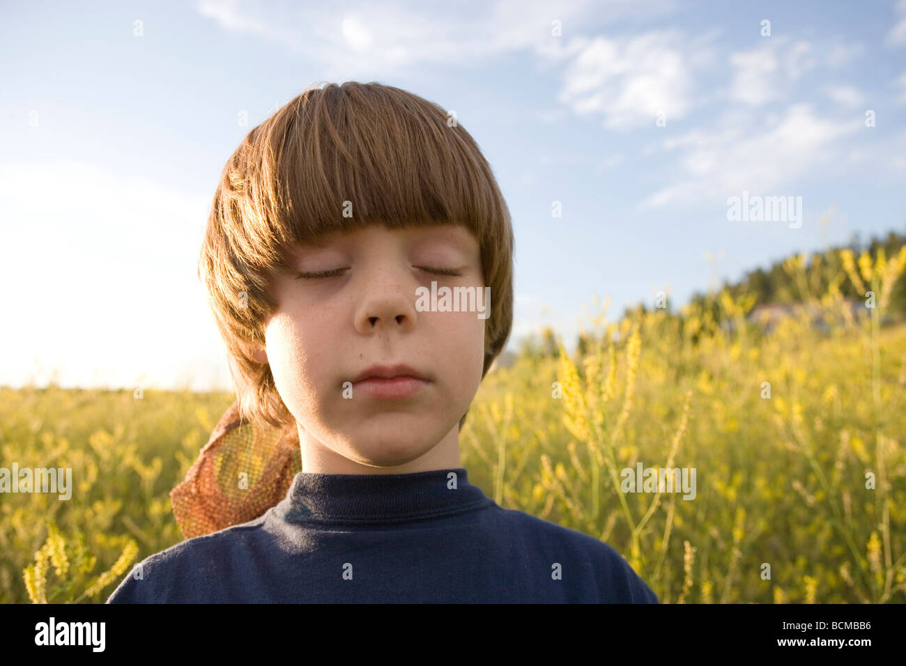 sieben Jahre alter Junge singen seine Augen schließen und hören die Vögel in einem Feld von Wildblumen, Pagosa Springs, Colorado Stockfoto