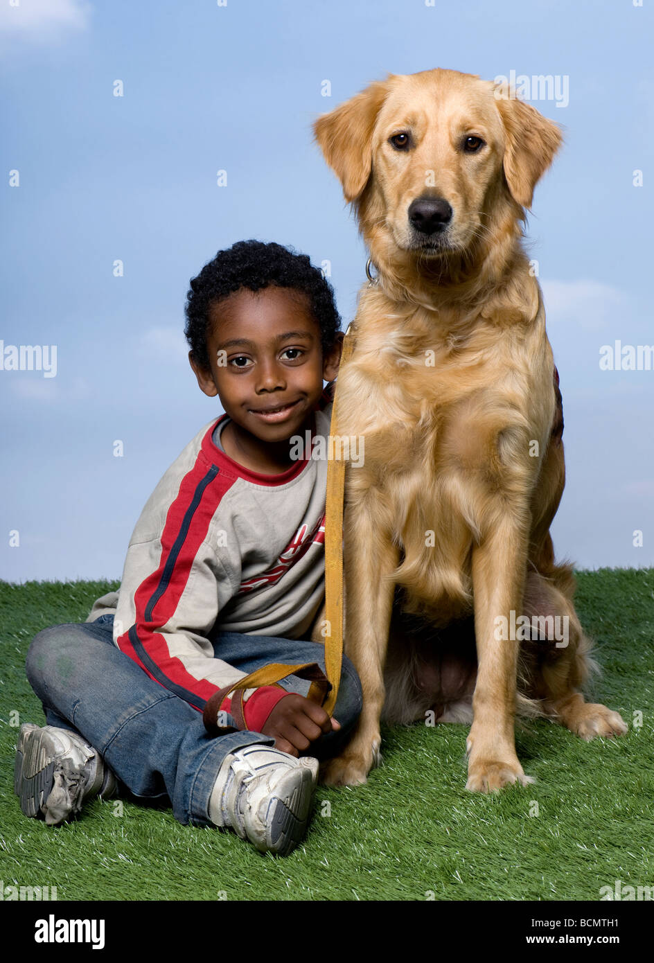 African American Boy und ein Golden Retriever, sitzen auf dem Rasen, 1 Jahr alt, vor blauem Himmel, Studio gedreht Stockfoto