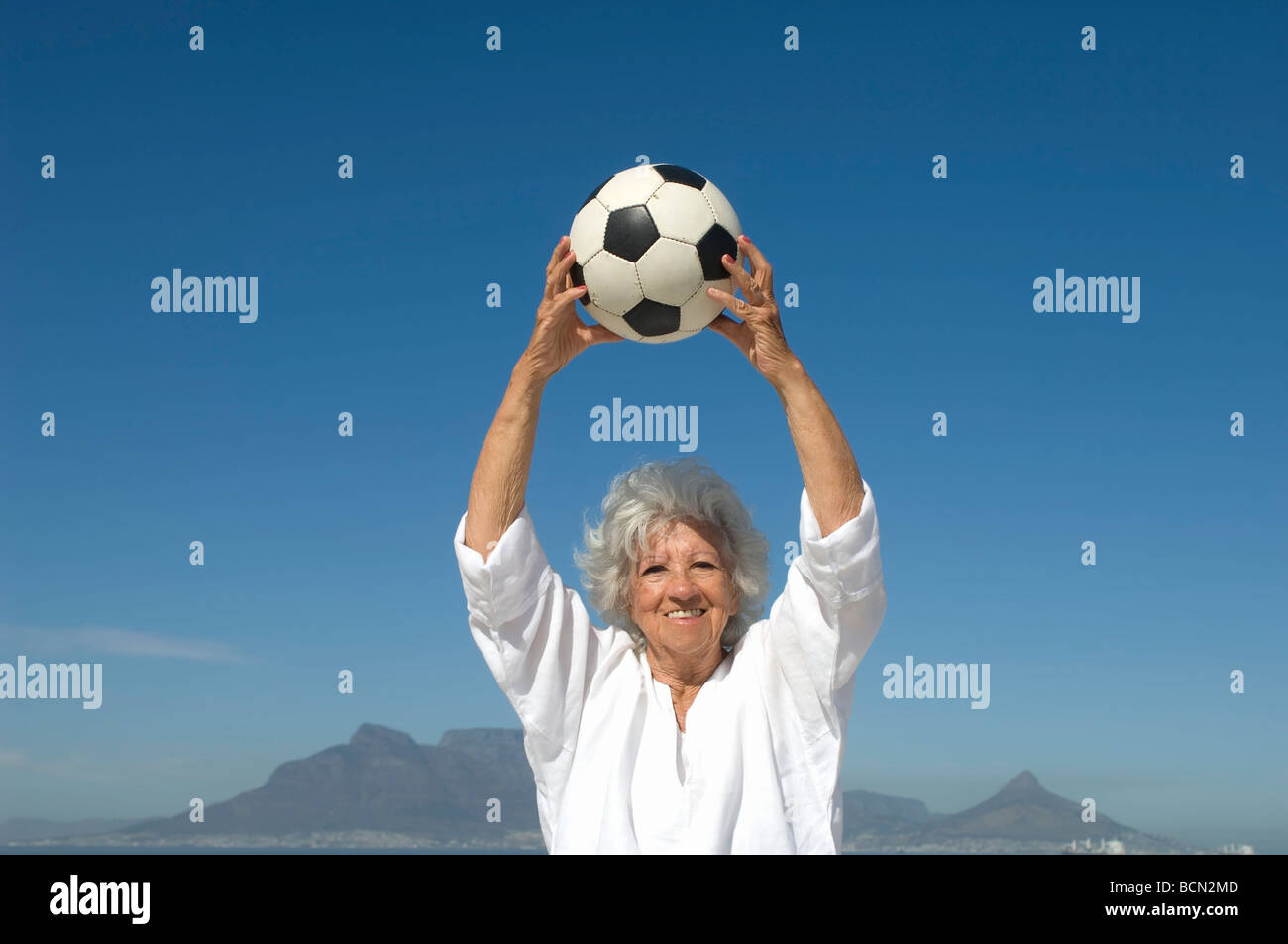 Ältere Frau hält Fußball über Kopf am Strand, Tafelberg im Hintergrund, Tabellenansicht Stockfoto