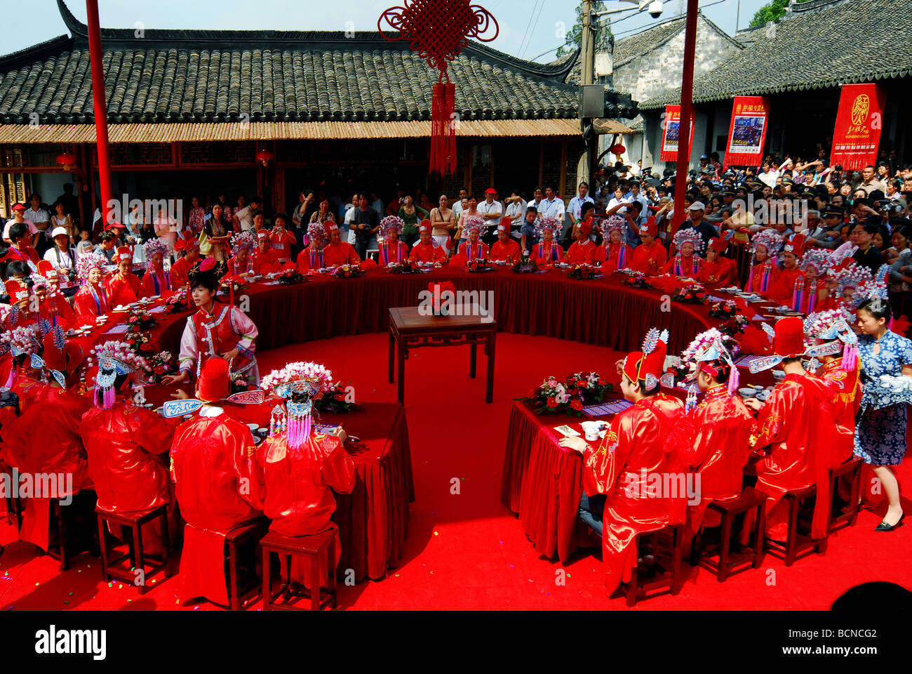 Braut und Bräutigam kleiden sich in traditionelle Brautkleid sitzen an einem runden Tisch in einer kollektiven Hochzeit, Shanghai, China Stockfoto