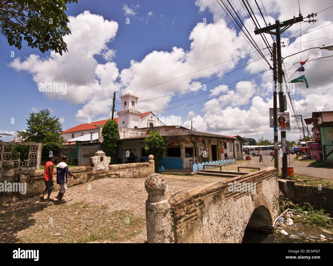 Einheimische Männer zu Fuß über eine Brücke im Zentrum von Portobello, Panama mit der Kirche San Felipe im Hintergrund Stockfoto