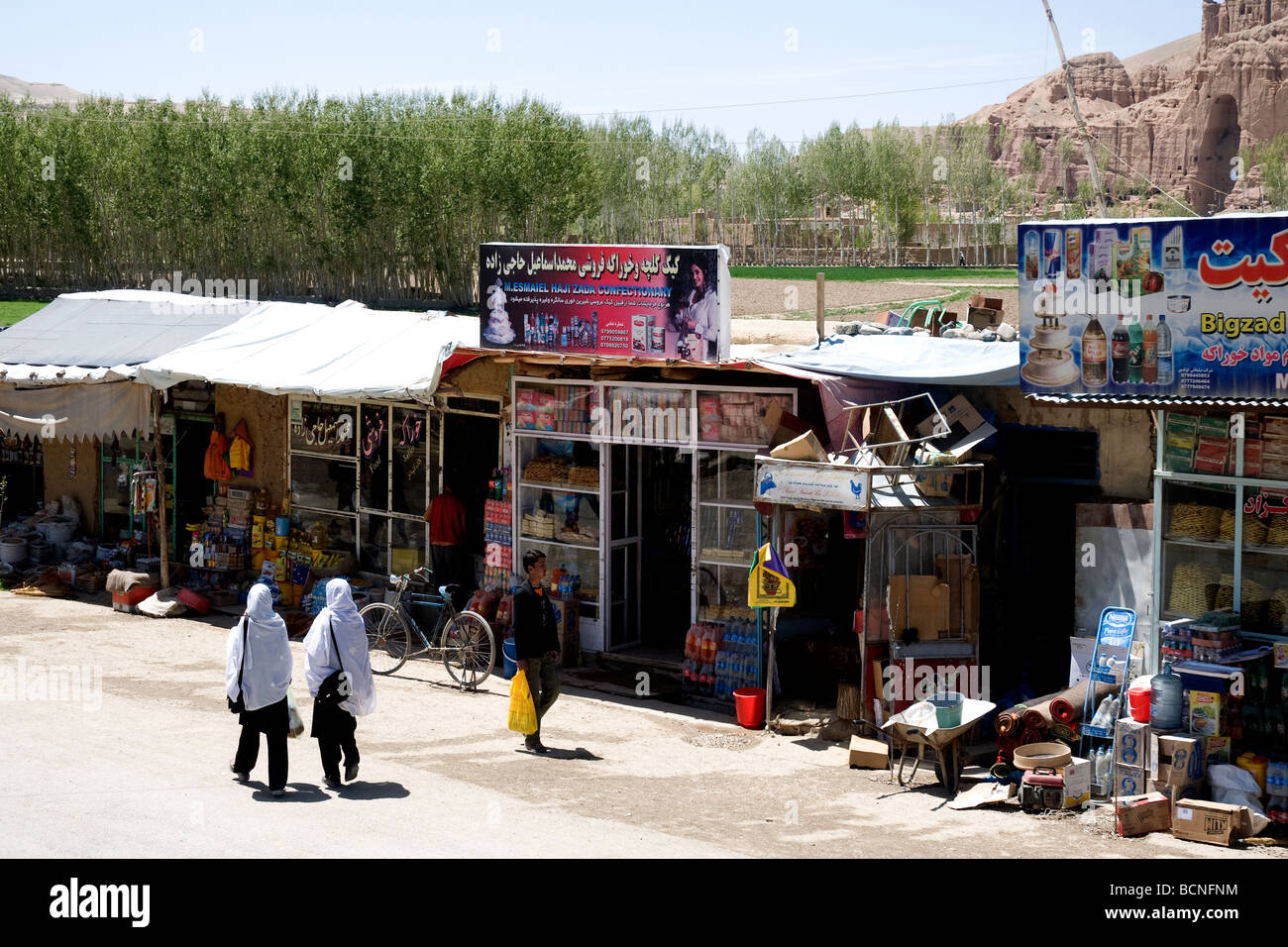 Zwei Weiß verhüllte Schülerinnen Fuß eine Straße entlang, vorbei an Geschäften Bamiyan, Afghanistan Stockfoto