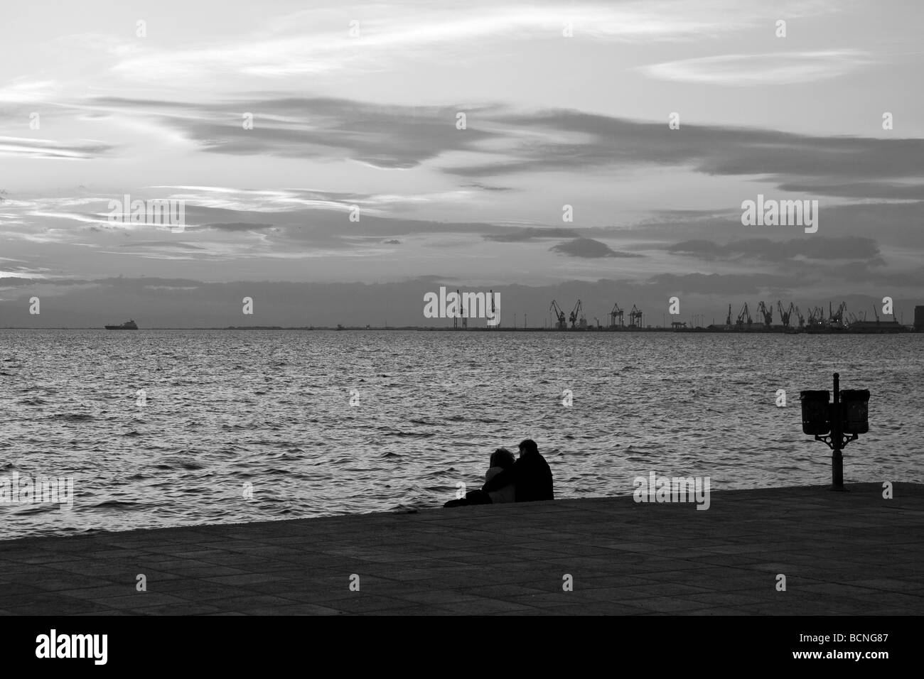 Ein paar sitzt am Meer am Nachmittag mit der Stadt im Hintergrund Stockfoto