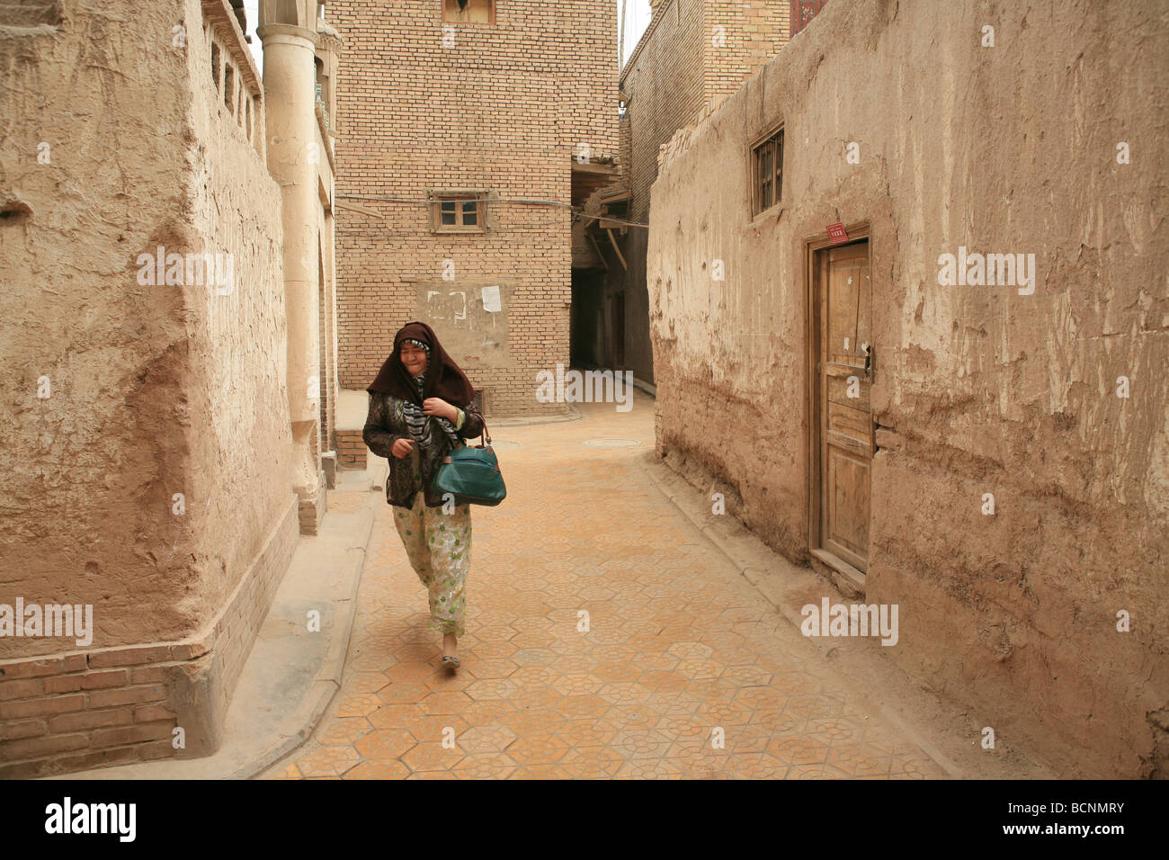 Uyghur Frau zu Fuß in enge Gasse der typischen Uyghur Wohngebiet bestehend aus Schlamm Ziegel Häuser, Hotan, Xinjiang Uyghur Stockfoto