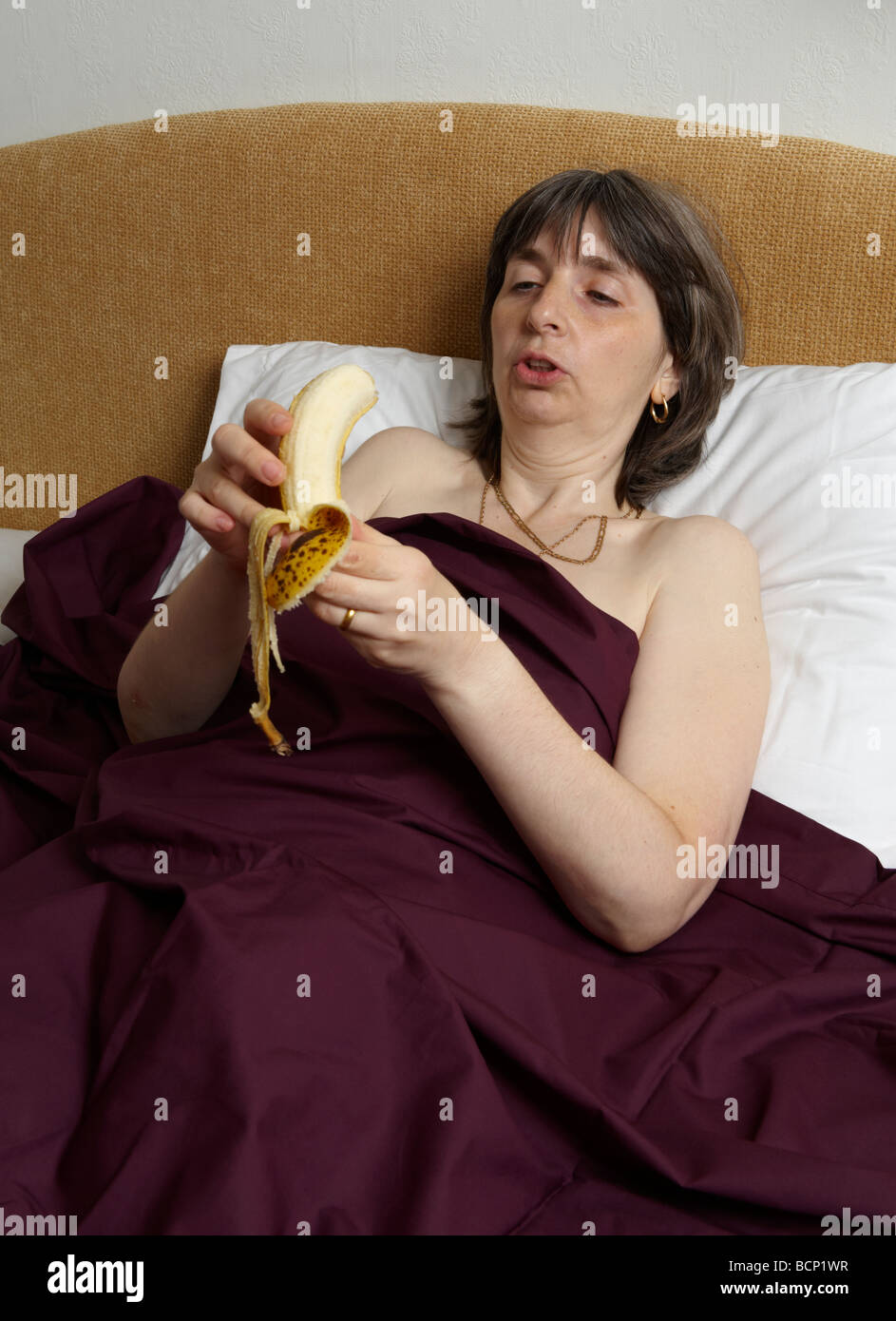 Applying Frau suggestiv im Bett liegend Banane essen Stockfoto