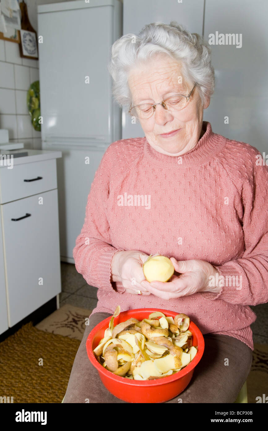 Frau in Ihren Siebzigern Sitzt in der Küche Und Schält Kartoffeln Stockfoto