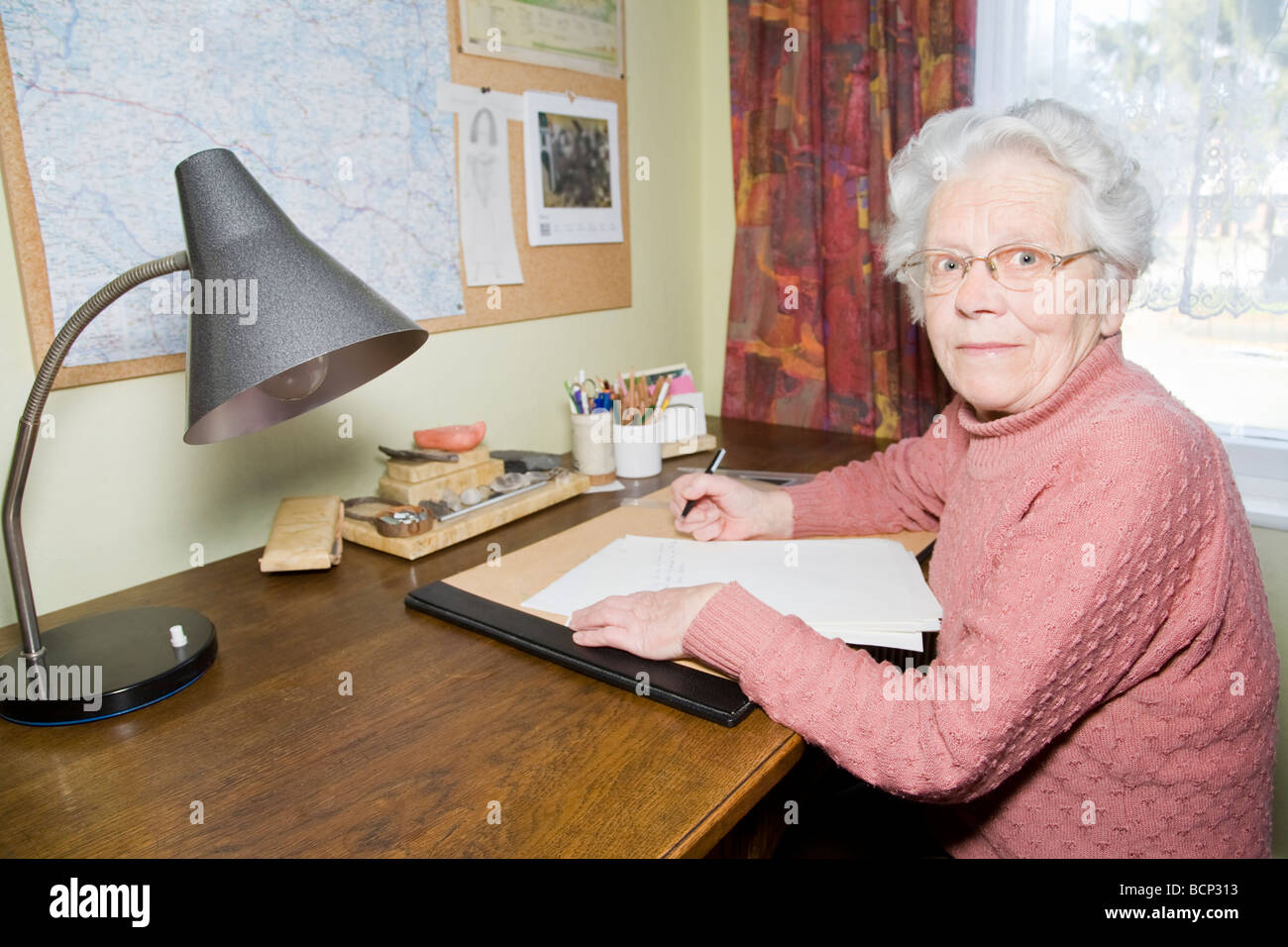 Frau in Ihren Siebzigern Sitzt bin Schreibtisch Und Schreibt Einen Brief Stockfoto
