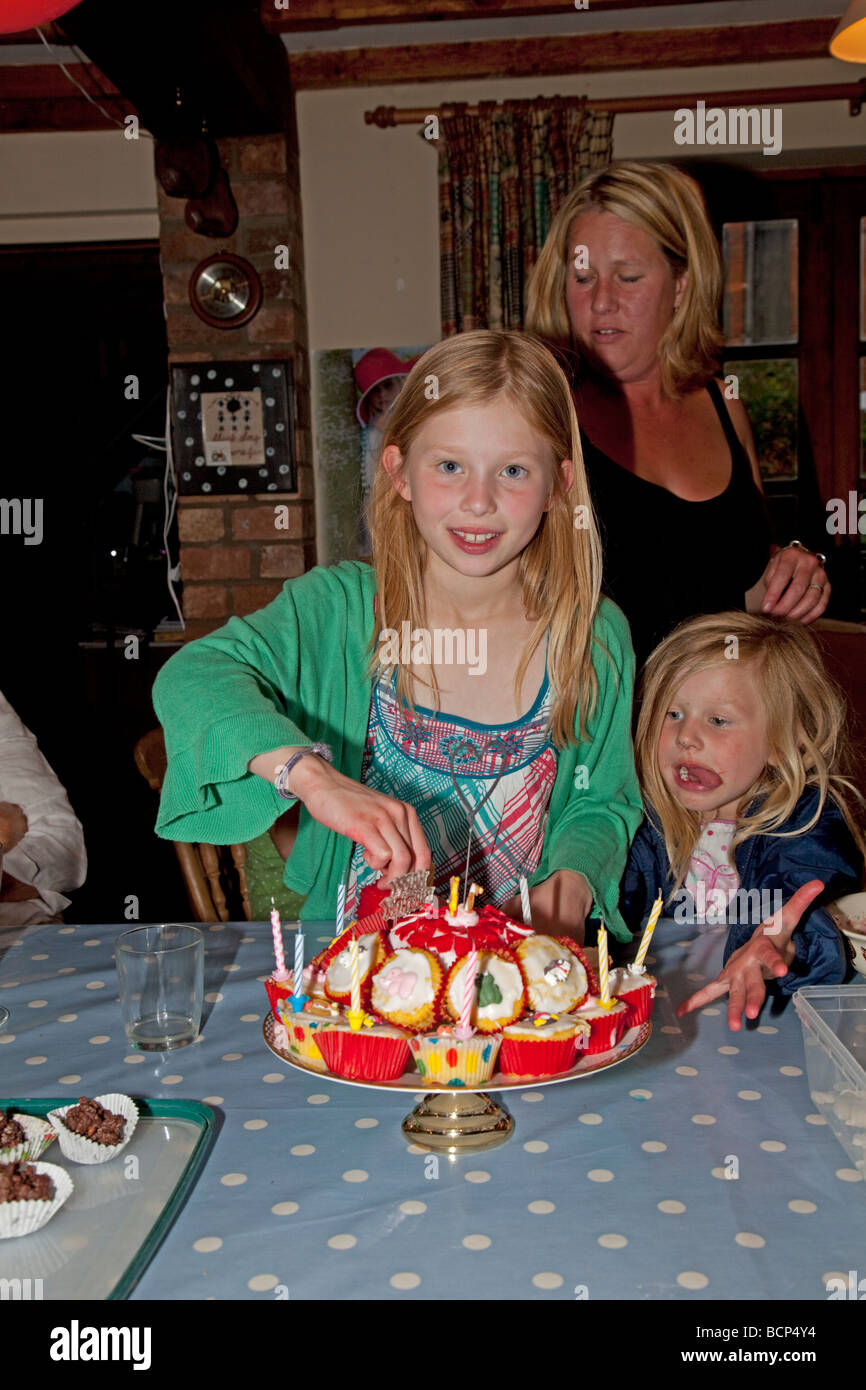Neun Jahre altes Mädchen mit Geburtstag Kuchen und hungrig jüngere Schwester Cotswolds UK Stockfoto