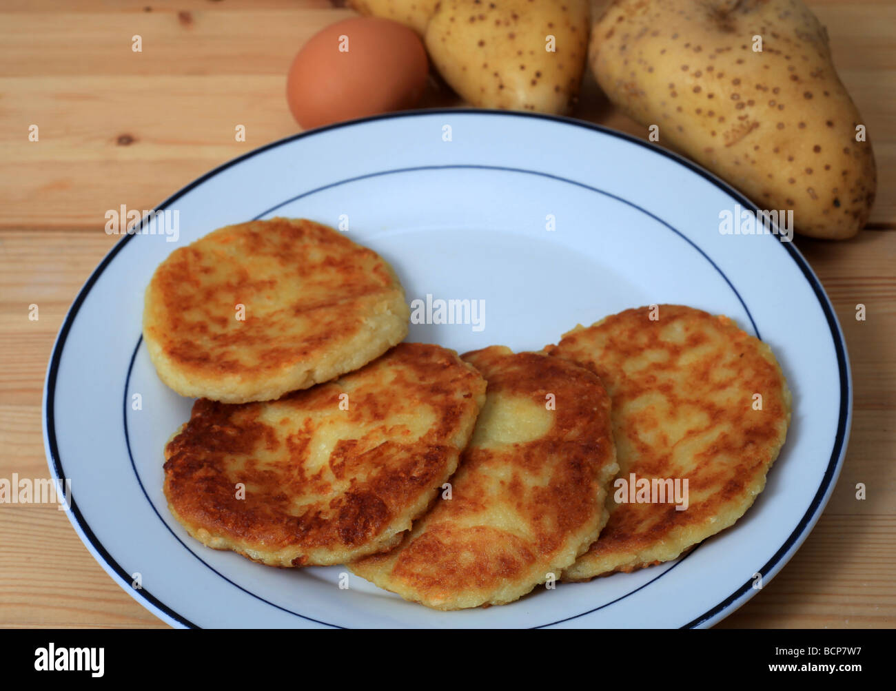 Ein Teller mit gebratenen Kartoffel-Pfannkuchen mit Kartoffeln und ein Ei auf einem Holztisch Stockfoto