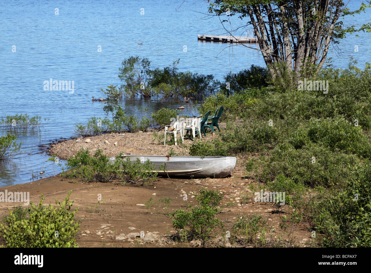 Eine alte Aluminium Ruderboot mit einigen sehr alten Plastikstühle am Ufer eines Sees, Adirondack. Stockfoto