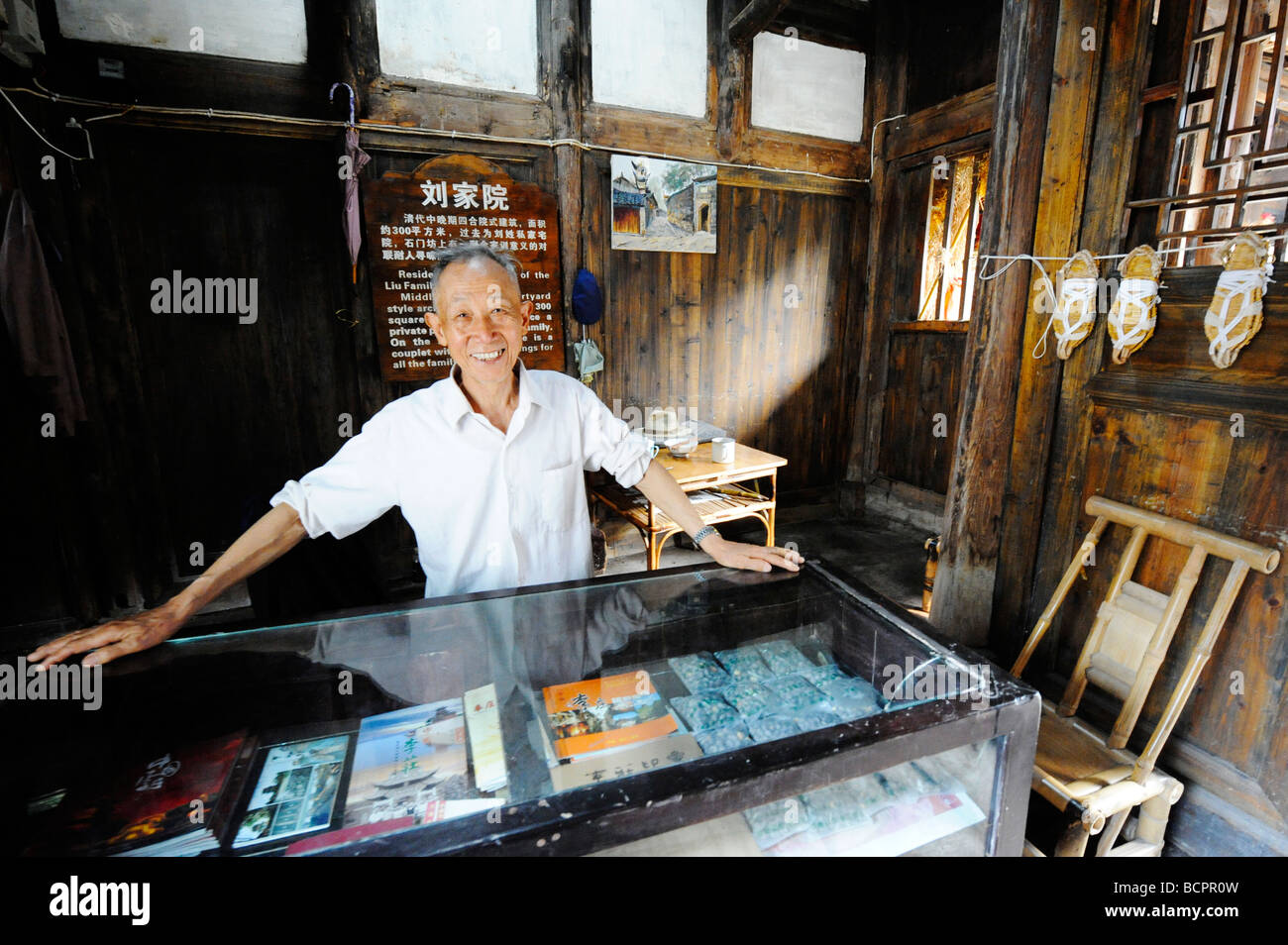 Ältere Menschen lächelnd Mann Chinesisch stand hinter der Theke ein Souvenir-Shop in Liu Familie Hof, Lizhuang die antike Stadt, Stockfoto