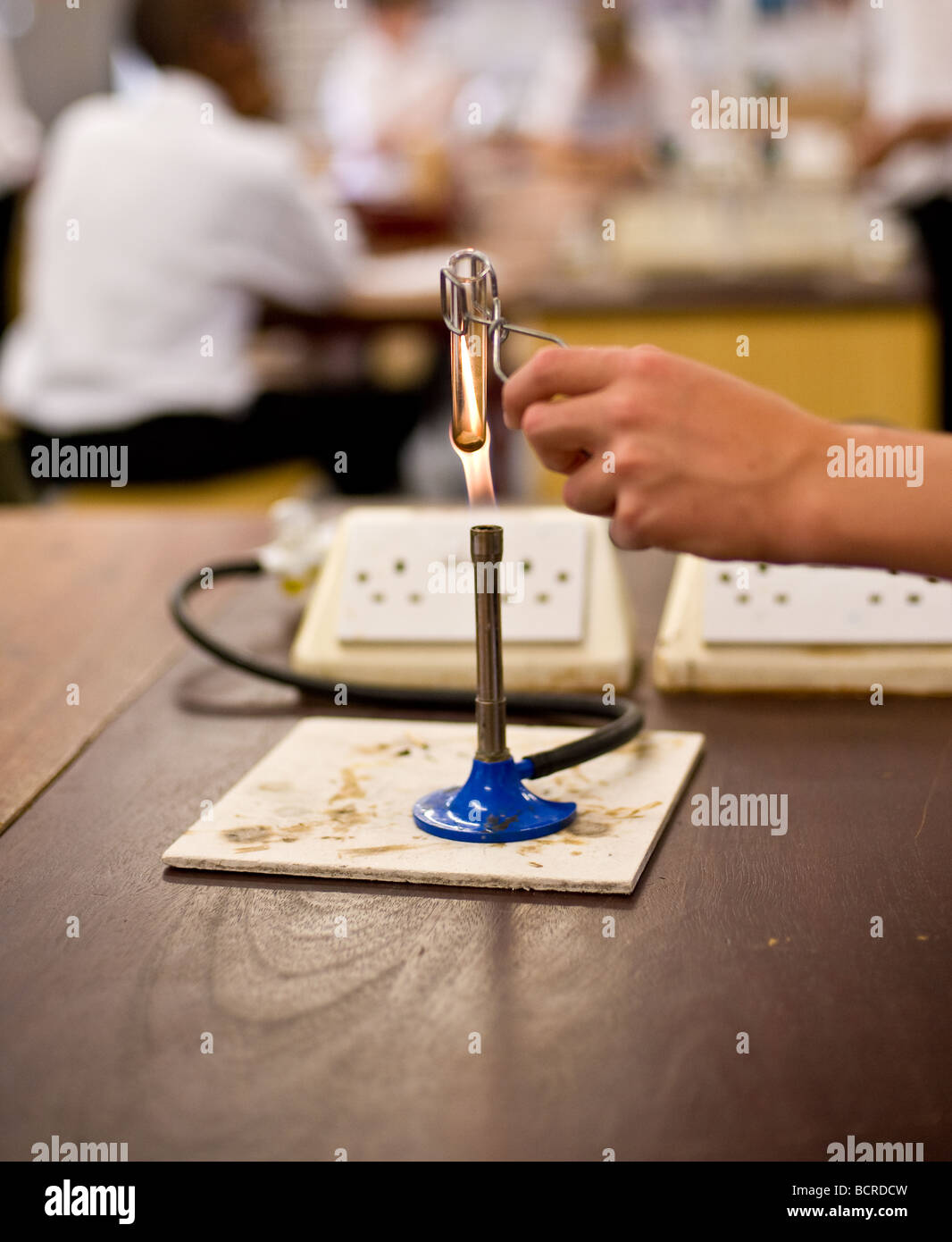 Ein Student Holding ein Reagenzglas über der Flamme eines Bunsenbrenners in einem Schullabor Stockfoto