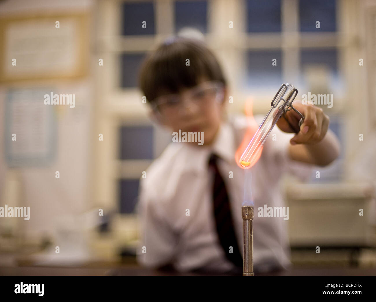 Britische Schule - EIN junger männlicher Schüler hält ein Reagenzglas über der Flamme eines bunsenbrenners in einem Wissenschaftsunterricht in einer Schule. Stockfoto