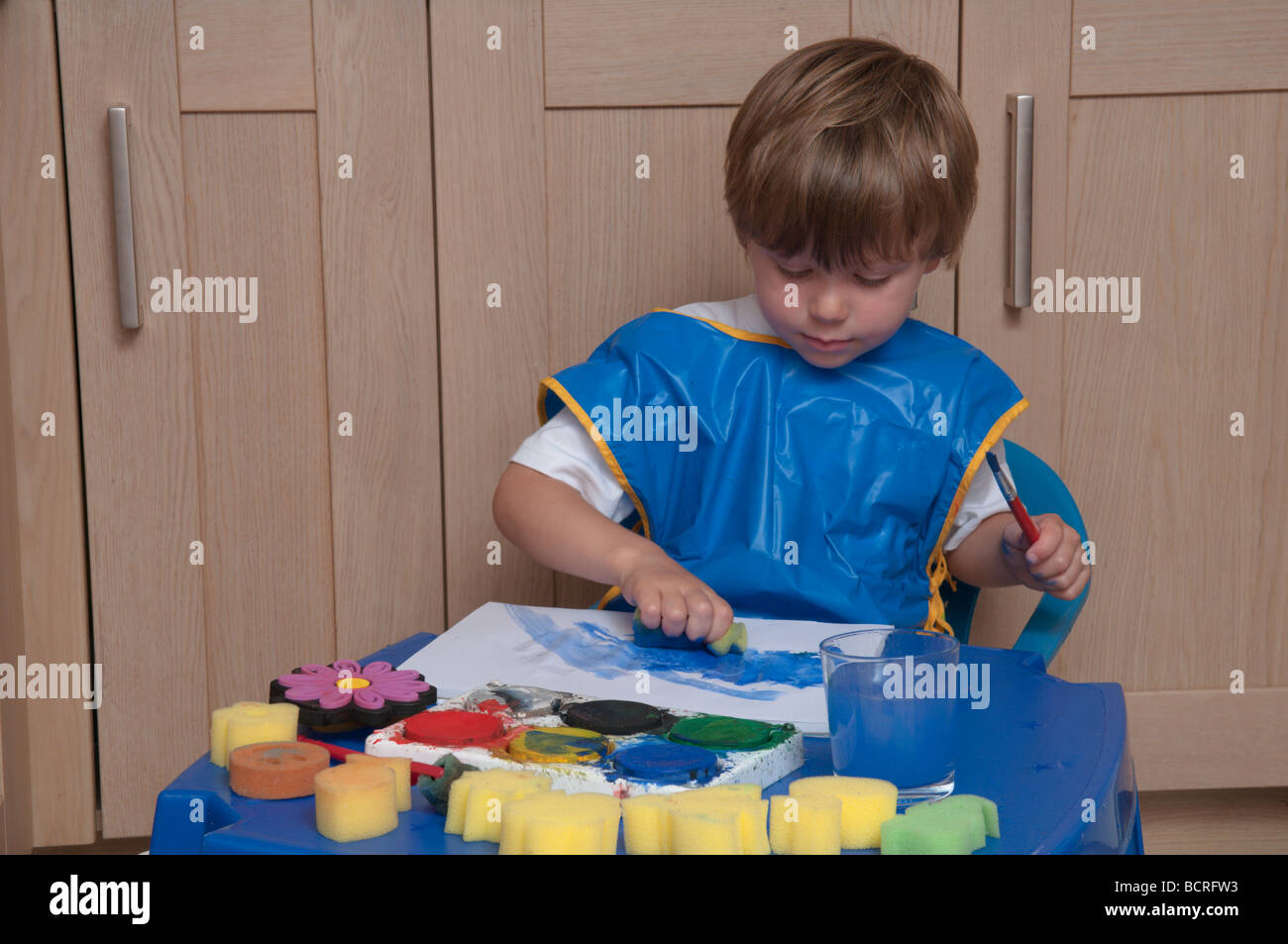 Drei Jahre alten Jungen an einem kleinen Tisch in der Küche spielen mit Pinsel und Schwämme, Kunst und Handwerk Stockfoto