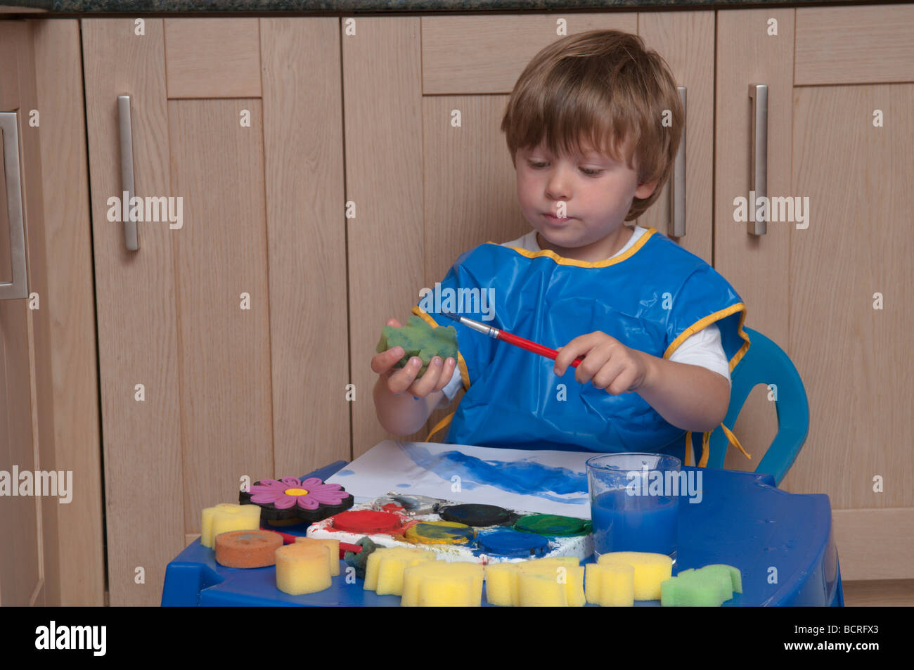 Drei Jahre alten Jungen an einem kleinen Tisch in der Küche spielen mit Pinsel und Schwämme, Kunst und Handwerk Stockfoto