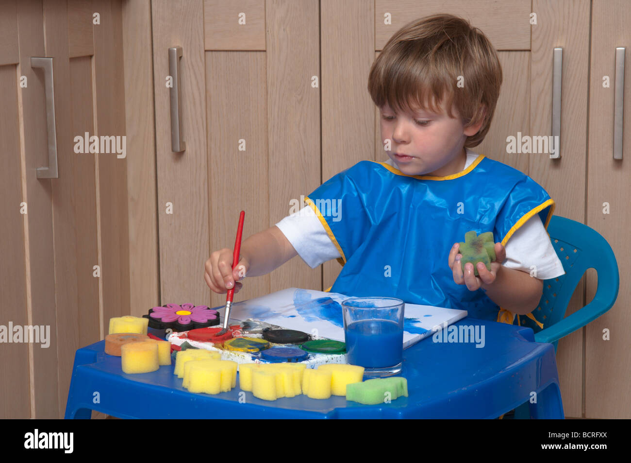 Drei Jahre alten Jungen an einem kleinen Tisch in der Küche spielen mit Pinsel und Schwämme, Kunst und Handwerk Stockfoto