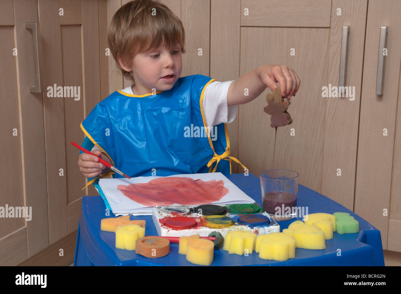 Drei Jahre alten Jungen an einem kleinen Tisch in der Küche spielen mit Pinsel und Schwämme, Kunst und Handwerk Stockfoto