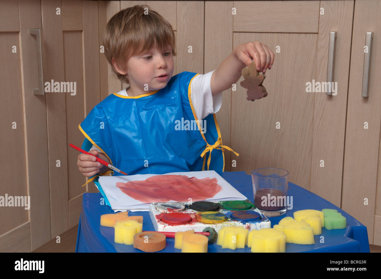 Drei Jahre alten Jungen an einem kleinen Tisch in der Küche spielen mit Pinsel und Schwämme, Kunst und Handwerk Stockfoto