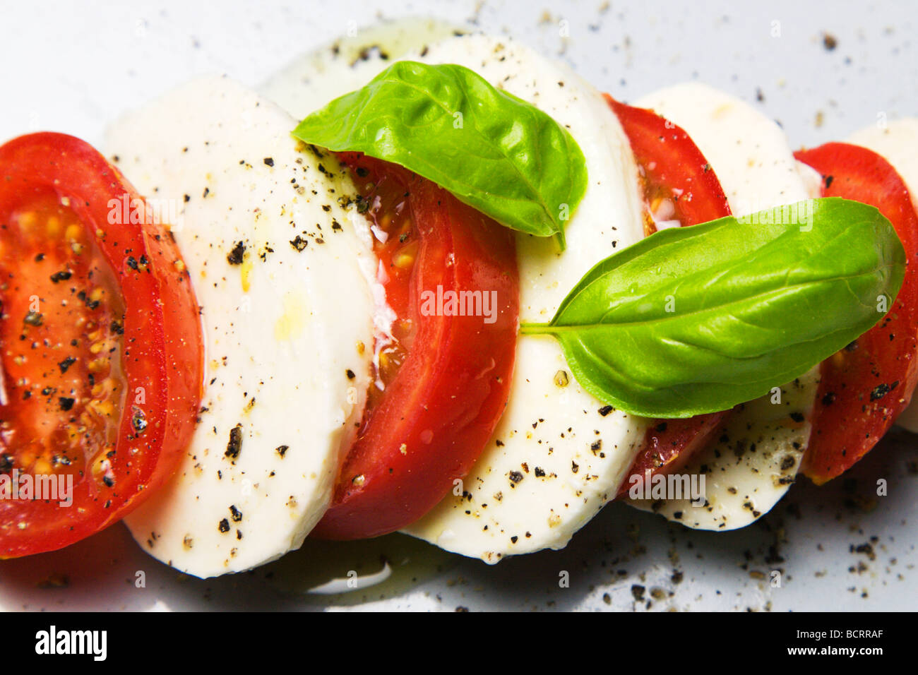 Tomaten und Mozzarella Salat mit frischem Basilikum Blätter schwarzer Pfeffer Stockfoto