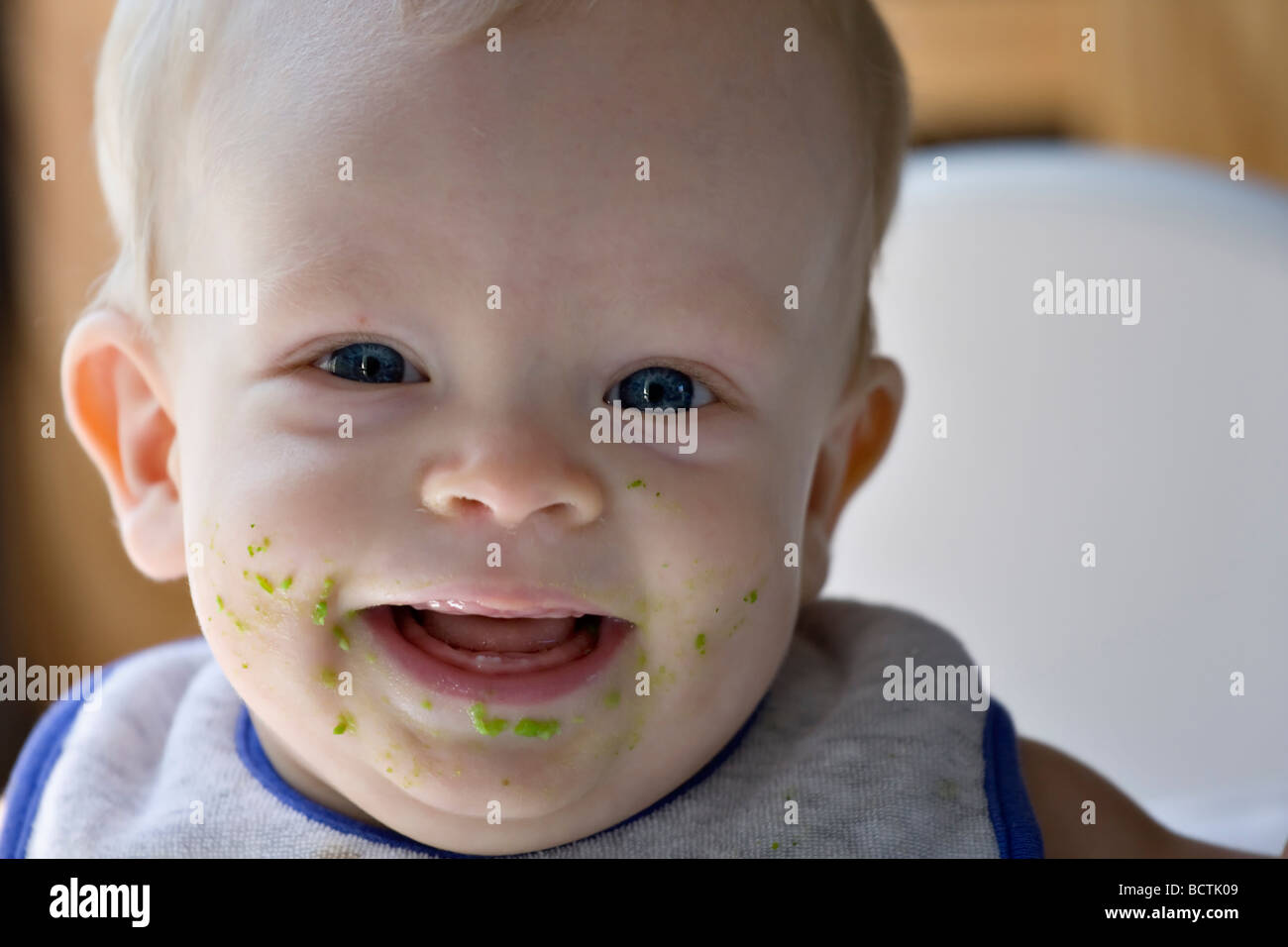 Sechs Monate altes Baby junge lächelnd nach Erbsen essen und sie auf seinem Gesicht trägt ein Lätzchen, Zähne zu zeigen. Stockfoto