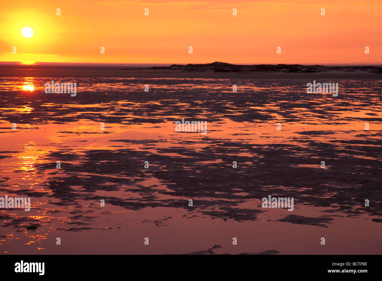 Sonne reflektiert über einen Fluss oder das Meer und der Sand am Strand bei Sonnenuntergang Stockfoto