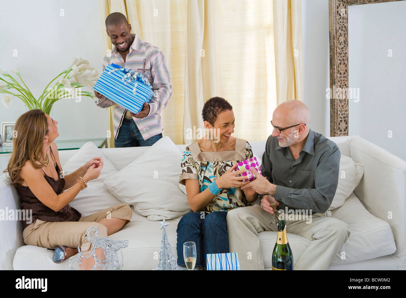 Mann hält ein Geschenk mit seinen drei Freunden auf einer Couch sitzend Stockfoto