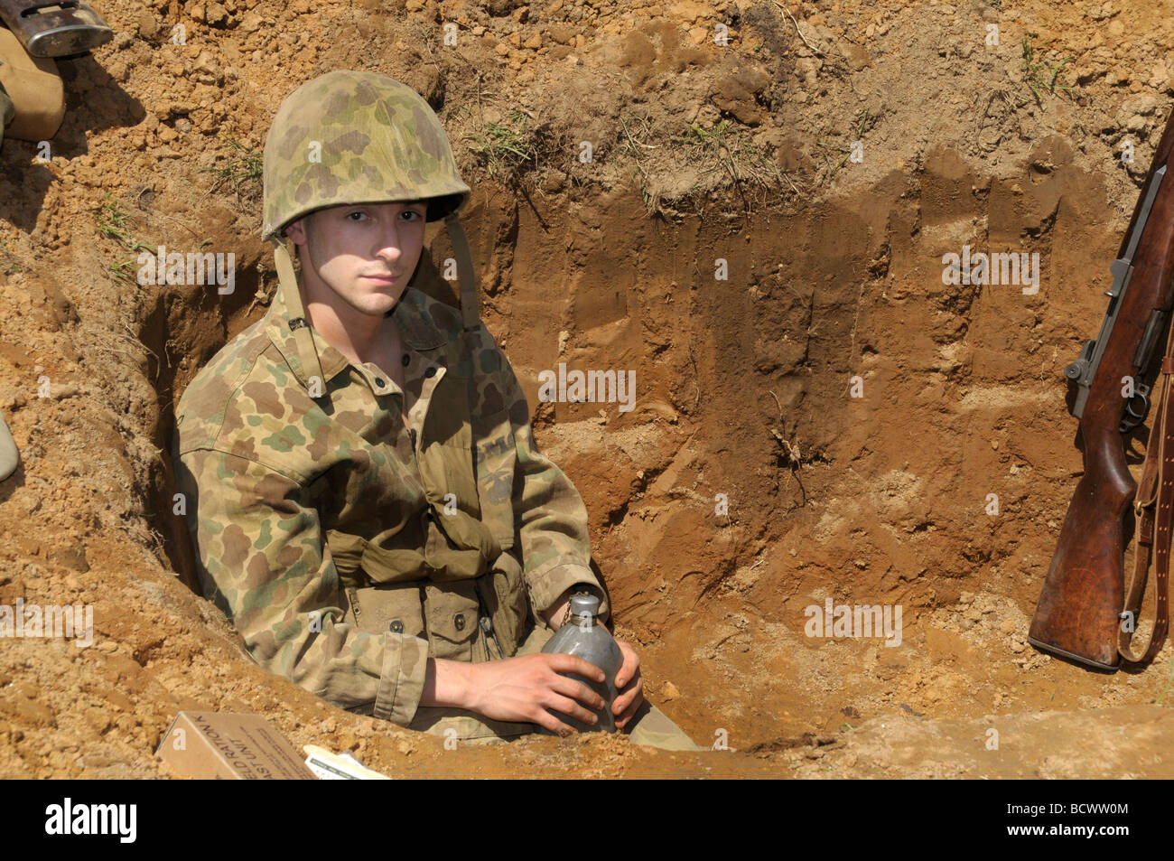 Mann, gekleidet wie ein Soldat in einem Erdloch während WWII Reenactment in Glendale, Maryland sitzt Stockfoto