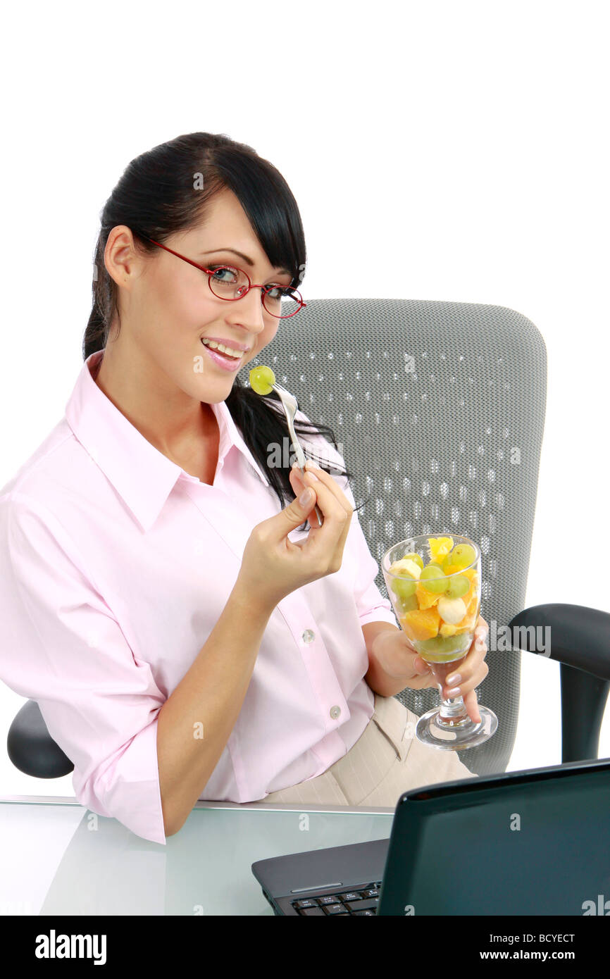 Junge Frau Isst Fruchtcocktail Im Buero junge Geschäftsfrau isst Obstsalat im Büro Stockfoto