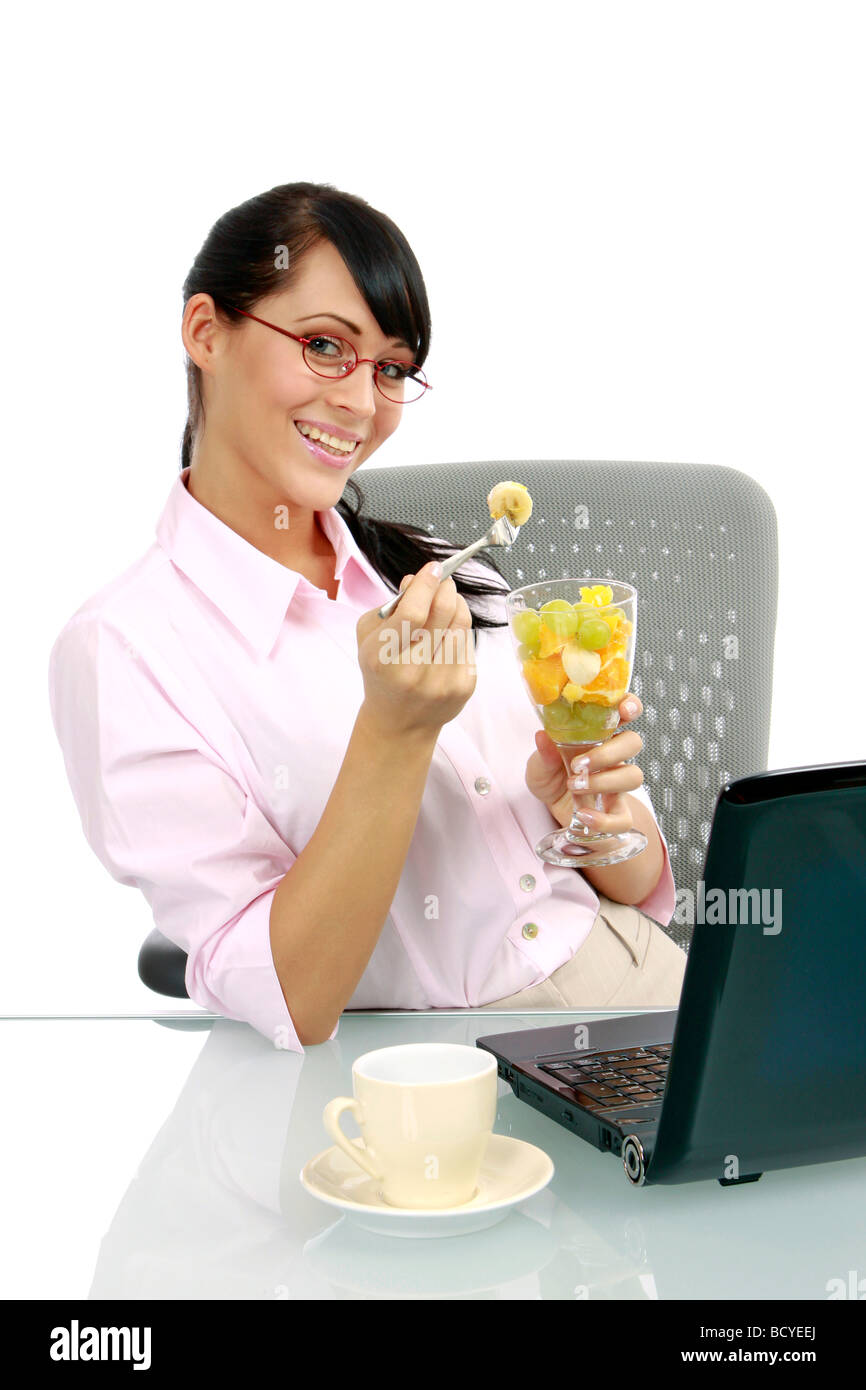 Junge Frau Isst Fruchtcocktail Im Buero junge Geschäftsfrau isst Obstsalat im Büro Stockfoto