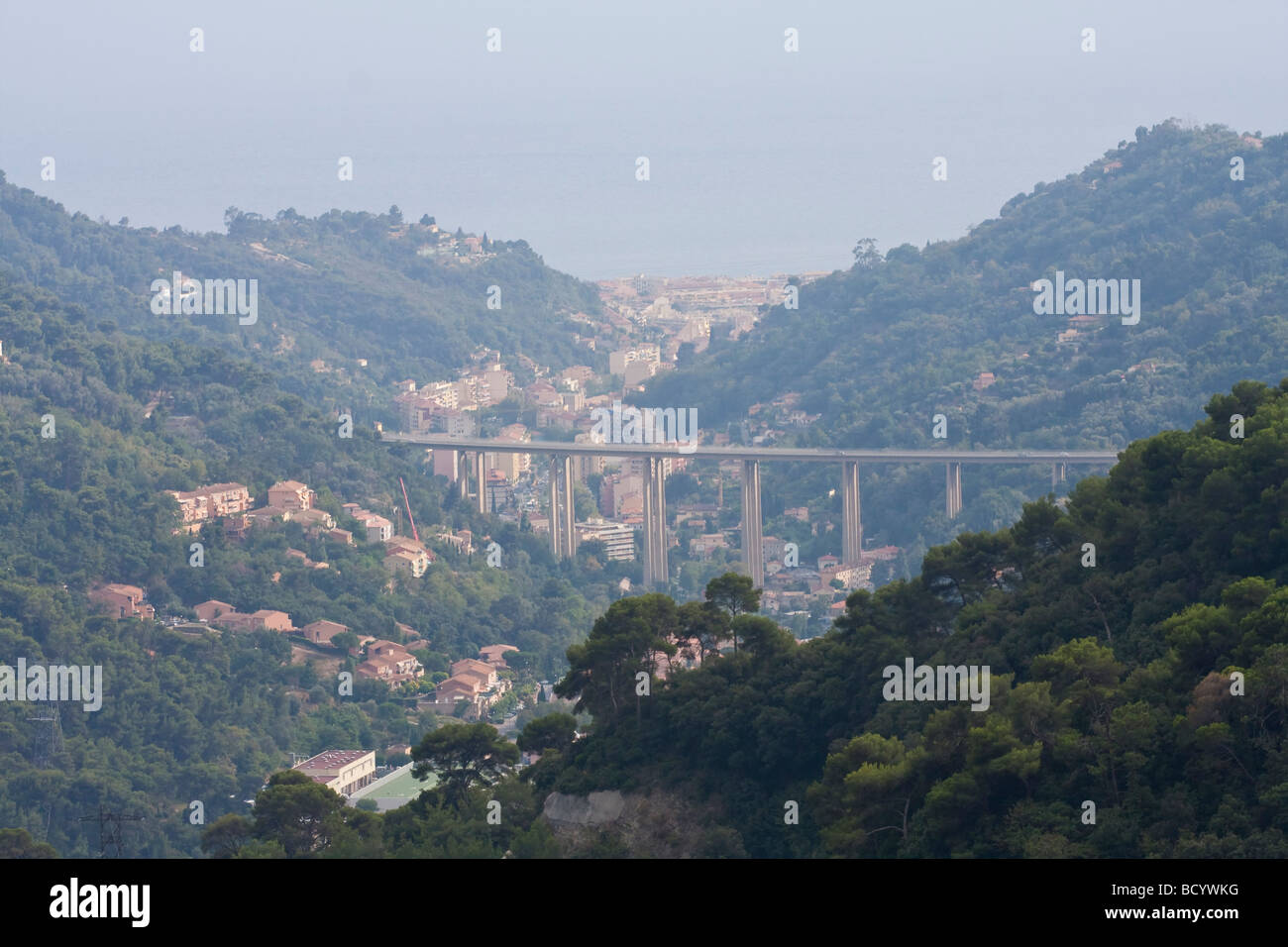 Erhöhter Blick auf ein nebeliges Tal mit einer modernen Brücke, umgeben von üppigem Grün in einer bergigen Landschaft. Stockfoto