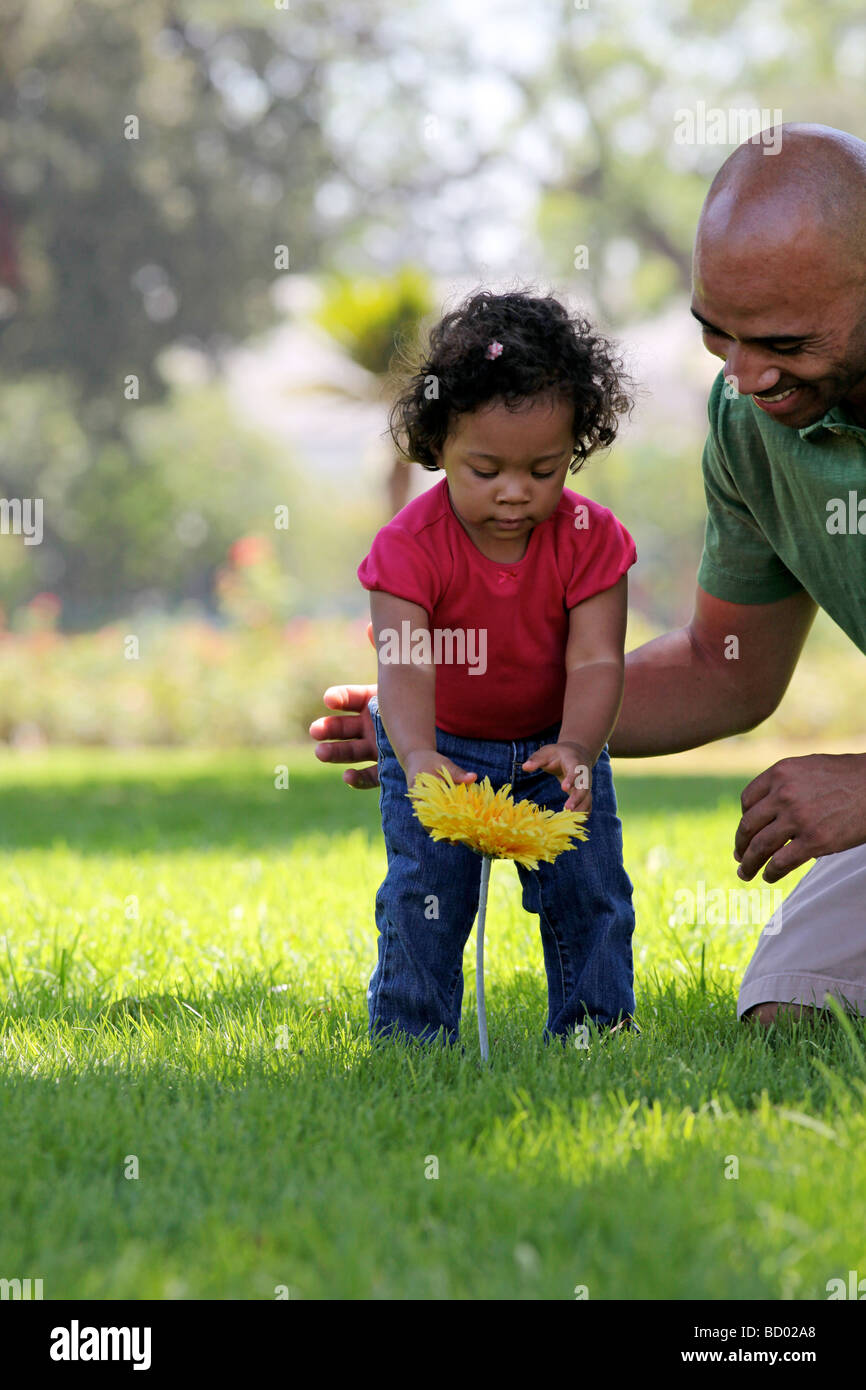 Papa und Kind spielen auf dem Rasen im Park mit einer gelben Blume Stockfoto