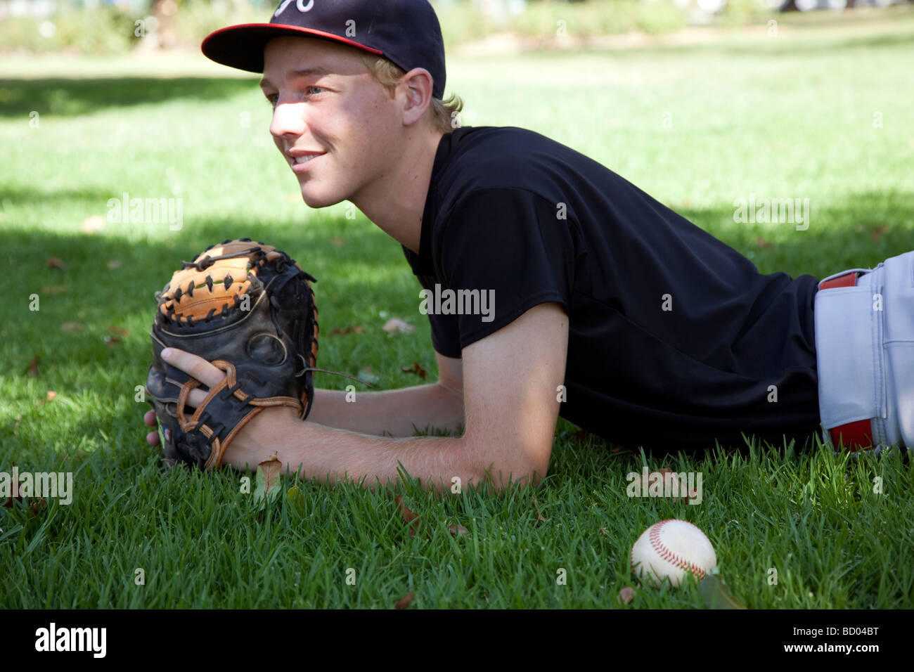 Teenager liegt auf dem Rasen mit base Ball und Catcher mit Stockfoto