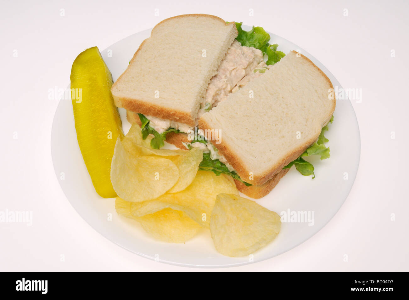 Thunfisch-Mayo-Sandwich auf Weißbrot mit Kartoffelchips und Gurke auf weißen Teller mit weißem Hintergrund, Stockfoto