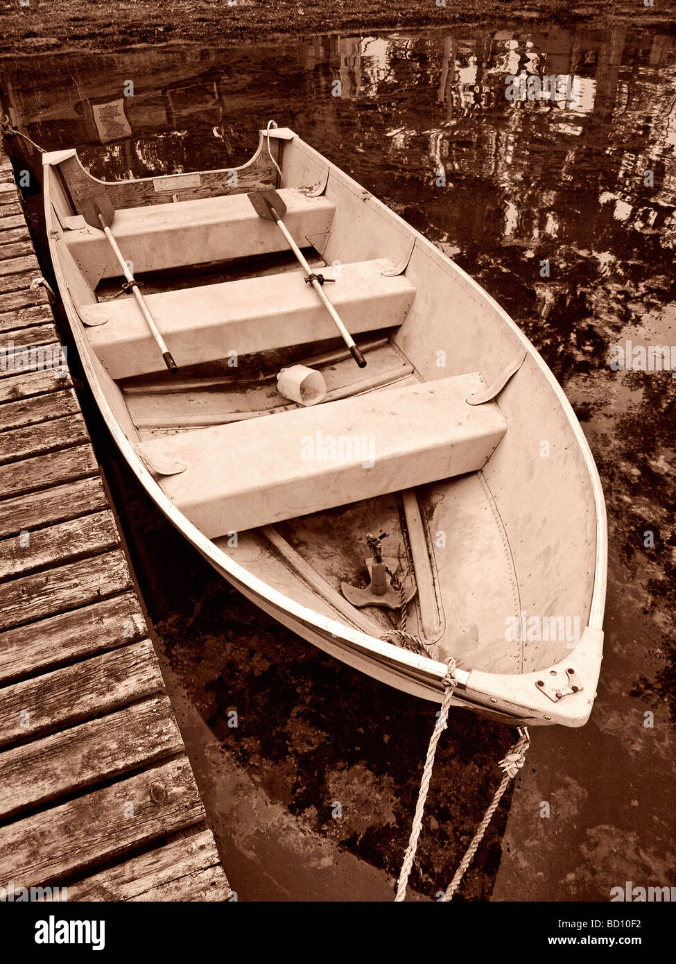 Ruderboot Boot an einem Dock an einem See mit Spiegelungen im Wasser und Ruder an Bord drei Sitze und in sepia Stockfoto