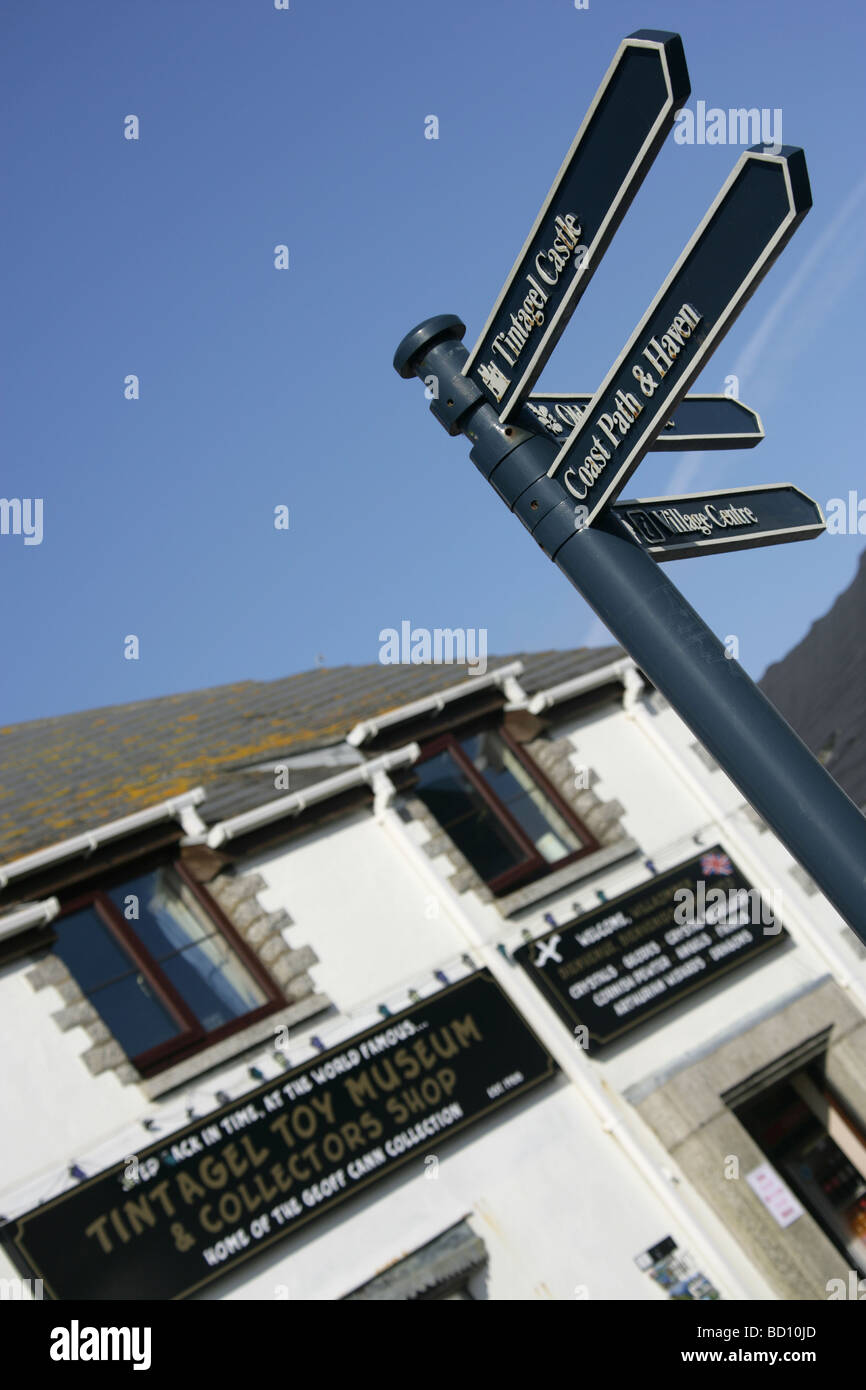 Dorf von Tintagel, England. Ein Besucher Wegweiser mit dem Spielzeugmuseum Tintagel und Sammler Shop im Hintergrund. Stockfoto