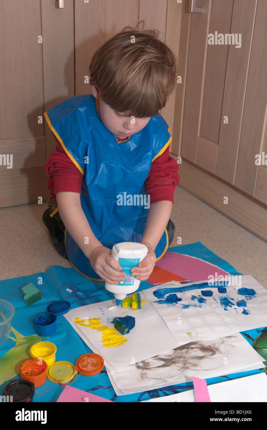 Kleiner Junge auf Küchenboden, der mit Pinseln, Schwämmen und Leimarbeiten spielt, kreativer Künstler, 3 Jahre alt Stockfoto