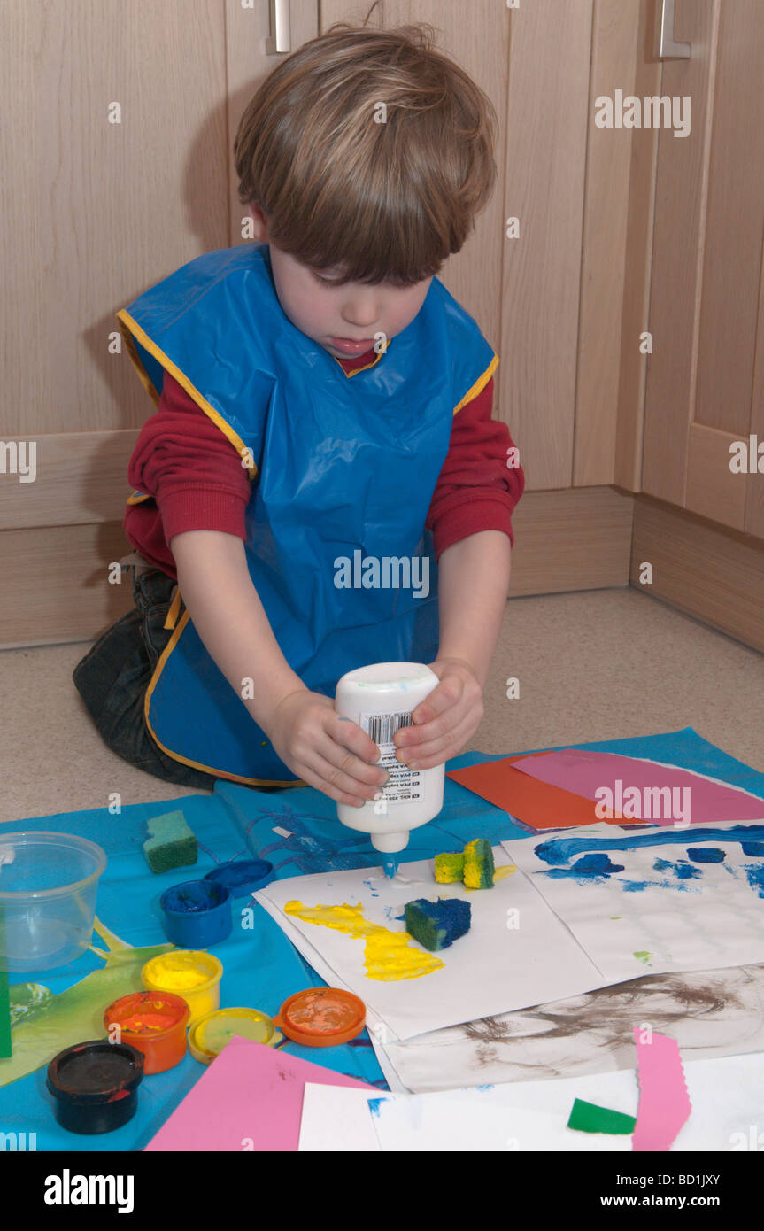 Kleiner Junge auf Küchenboden, der mit Pinseln, Schwämmen und Leimarbeiten spielt, kreativer Künstler, 3 Jahre alt Stockfoto