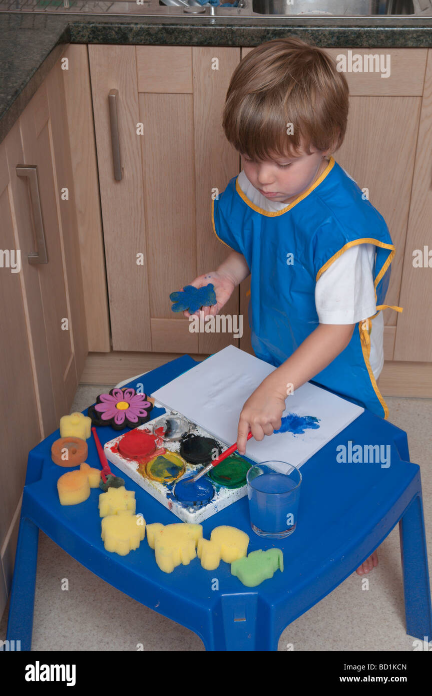 Junge, der kreativ und künstlerisch mit Pinseln und Schwämmen auf farbigem Papier spielt, drei Jahre alt Stockfoto