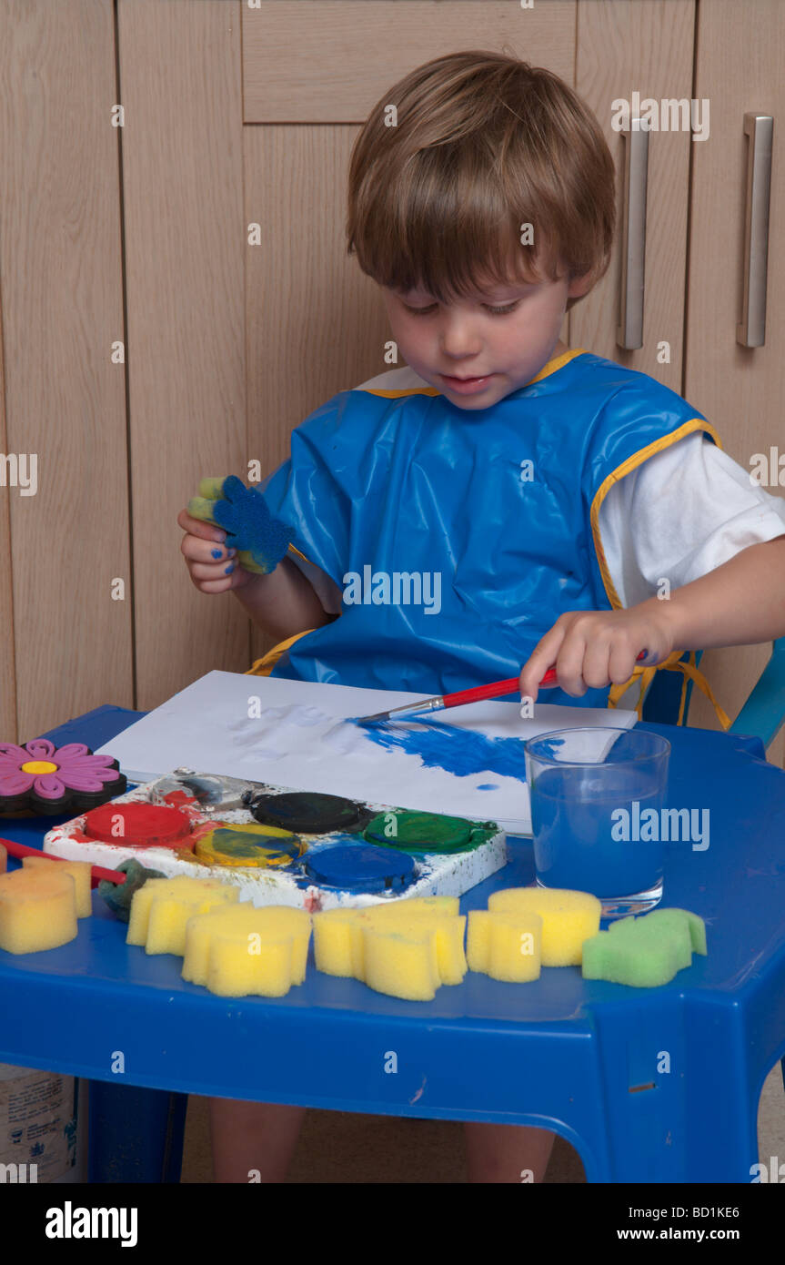Junge, der kreativ und künstlerisch mit Pinseln und Schwämmen auf farbigem Papier spielt, drei Jahre alt Stockfoto
