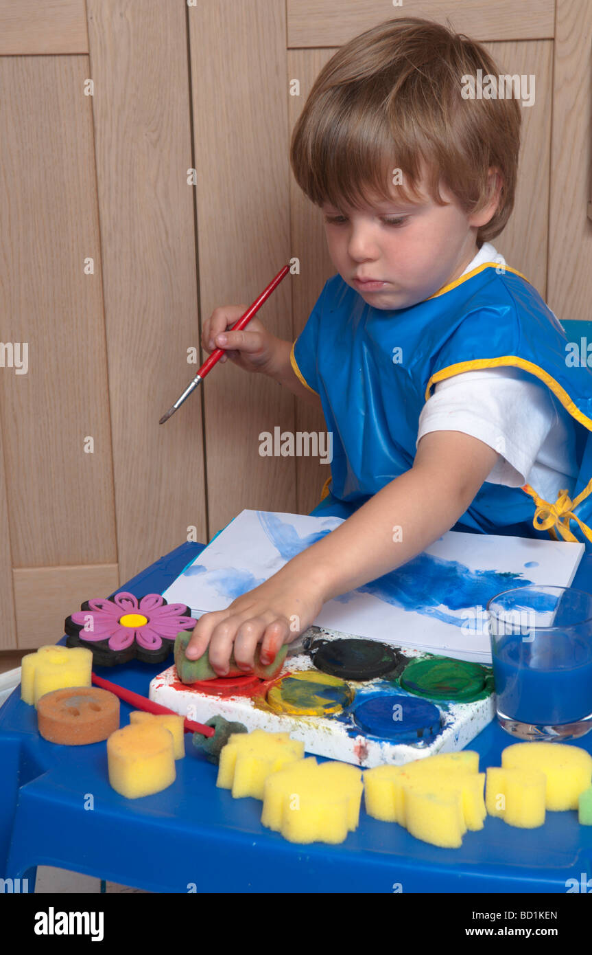 Junge, der kreativ und künstlerisch mit Pinseln und Schwämmen auf farbigem Papier spielt, drei Jahre alt Stockfoto