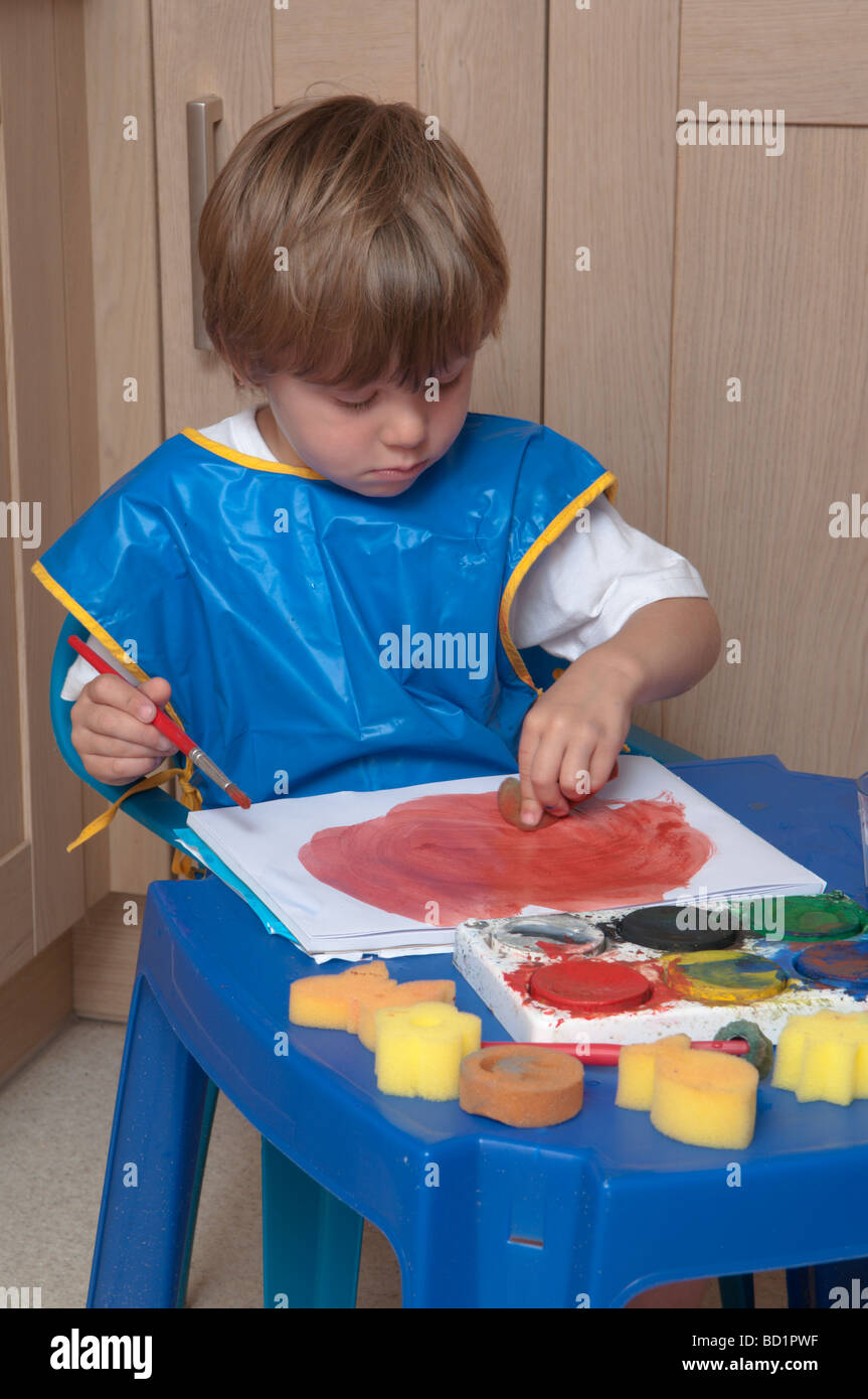 Junge, der kreativ und künstlerisch mit Pinseln und Schwämmen auf farbigem Papier spielt, drei Jahre alt Stockfoto